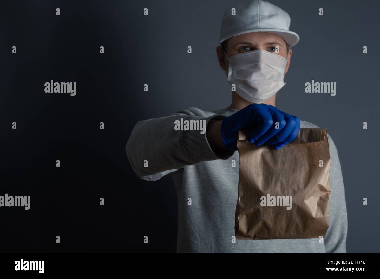 Livraison sûre de nourriture ou de marchandises. Un jeune courrier livrant une petite commande de sac en papier brun ECO à la maison du client avec masque et gants pendant le coronavi Banque D'Images