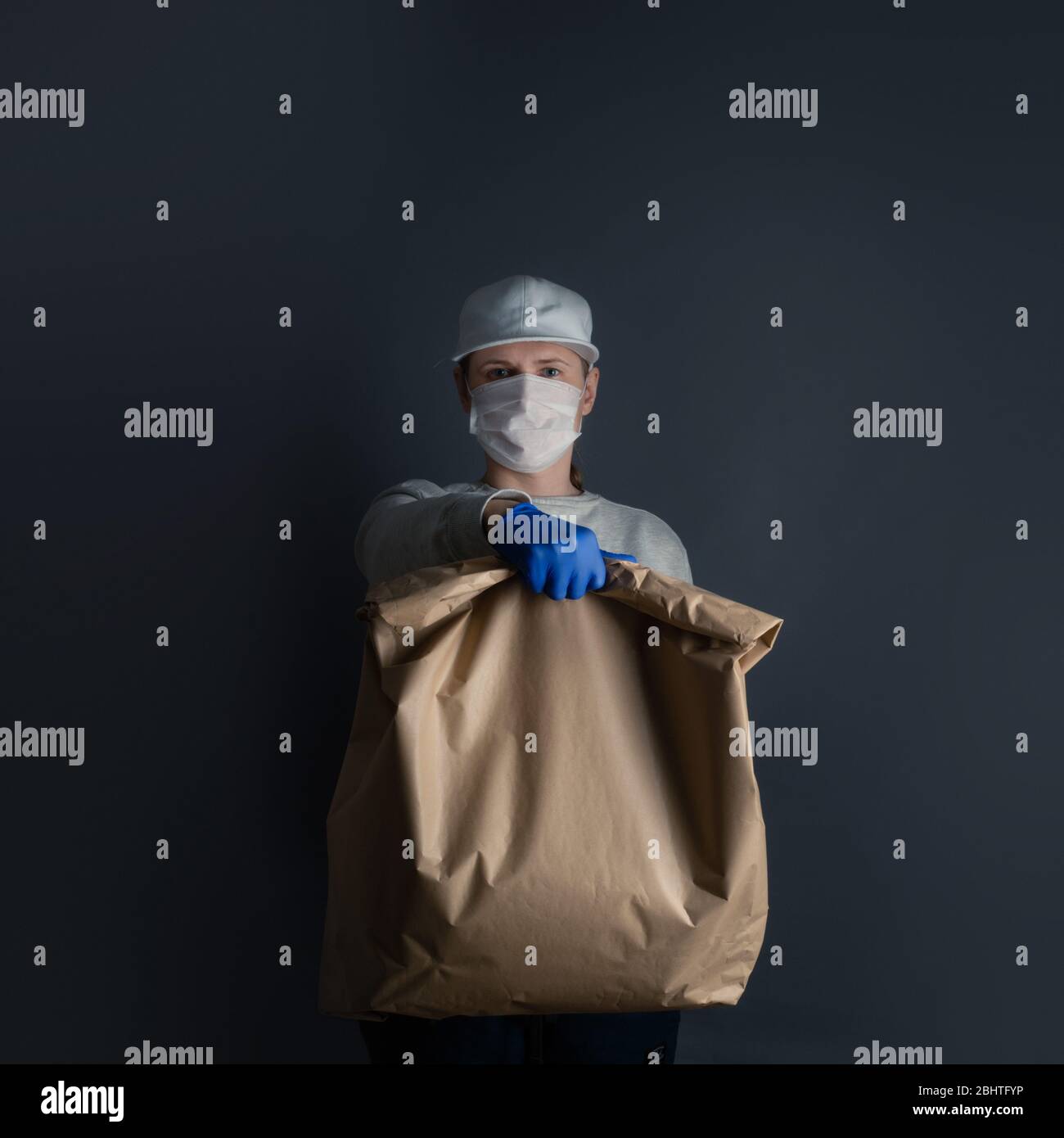 Livraison sûre de nourriture ou de marchandises. Un jeune transporteur livre à la maison du client une grosse commande de sacs en papier vert brun avec masque et gants pendant la co Banque D'Images