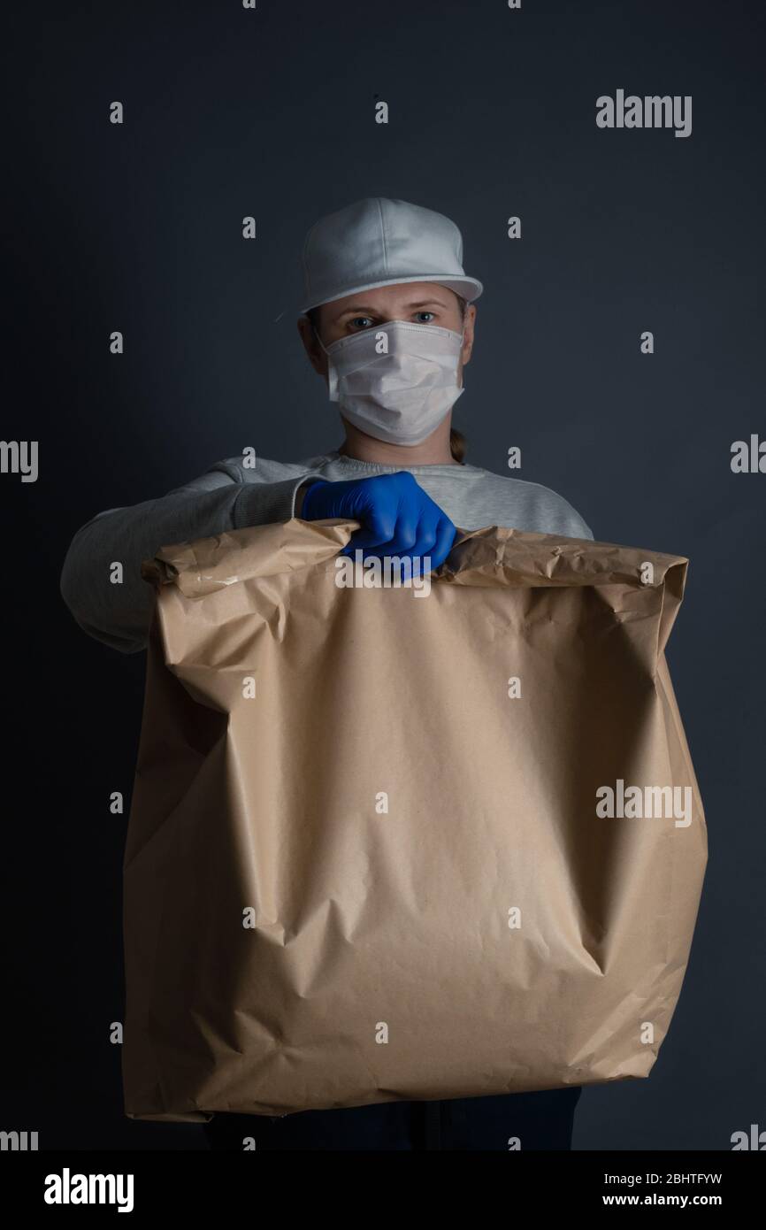 Livraison sûre de nourriture ou de marchandises. Un jeune transporteur livre à la maison du client une grosse commande de sacs en papier vert brun avec masque et gants pendant la co Banque D'Images