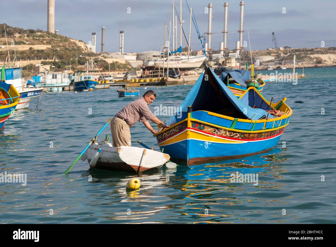 Homme qui tend le bateau de pêche luzzo traditionnel, Marsaxlokk, Malte Banque D'Images