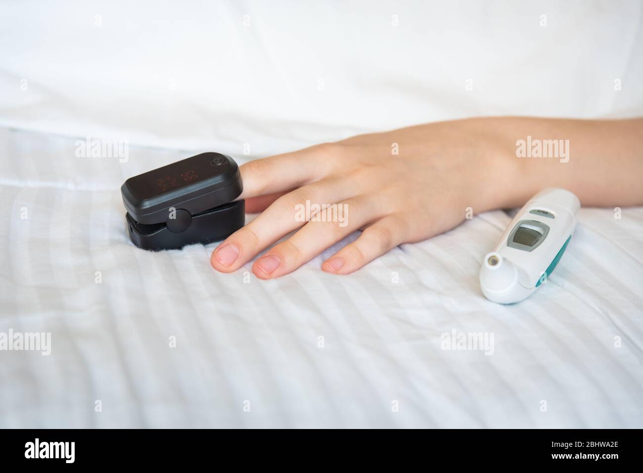 La main de la femme repose sur le lit avec un thermomètre numérique et porte l'oxymètre de pouls sur le doigt Banque D'Images