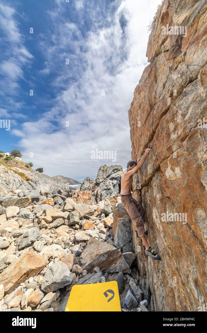 Grimpeur de roche mâle pratiquant le boulandrage sans corde sur un bloc devant la mer. Un bloc élevé pour les gens avec ténacité et confiance Banque D'Images