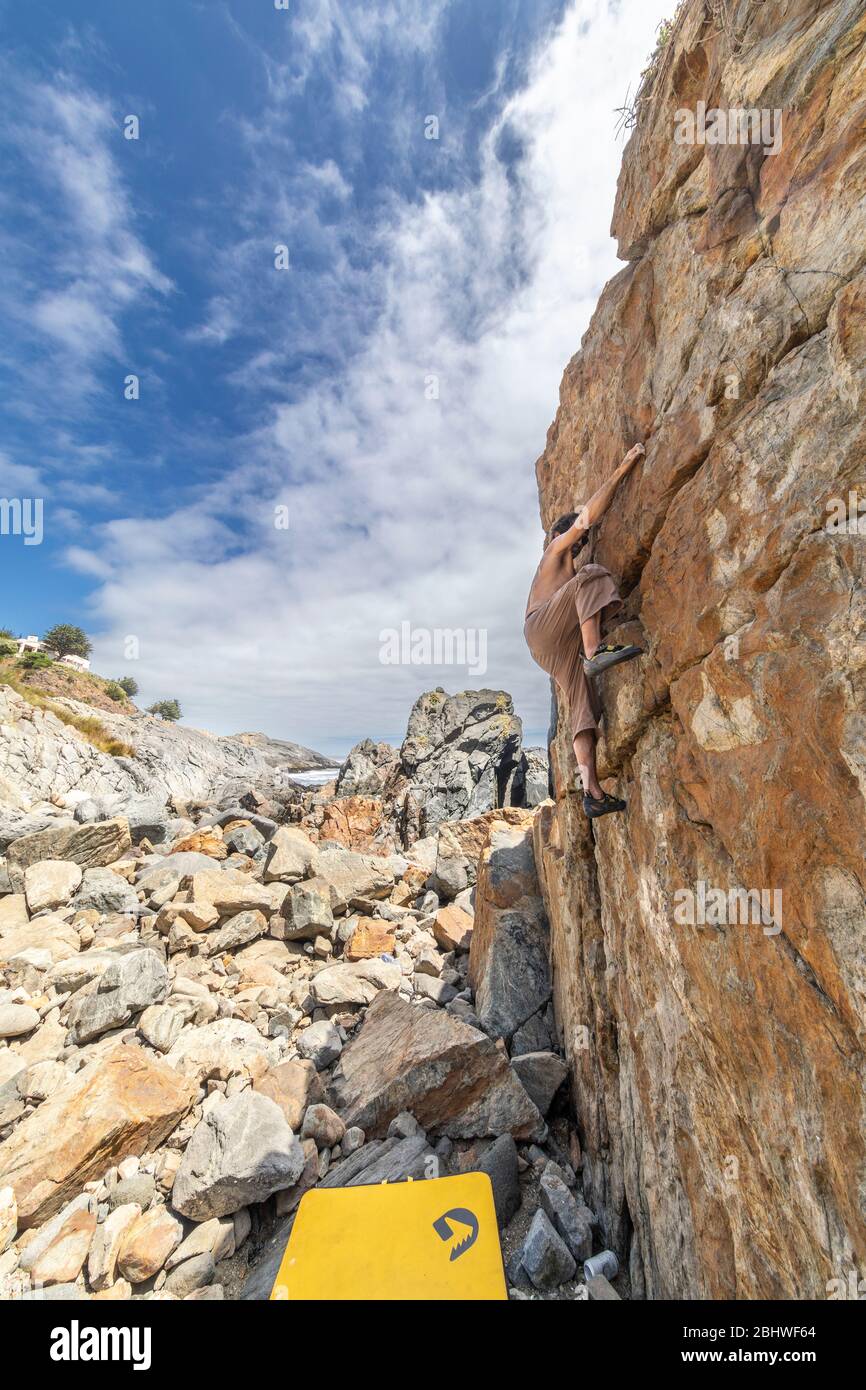 Grimpeur de roche mâle pratiquant le boulandrage sans corde sur un bloc devant la mer. Un bloc élevé pour les gens avec ténacité et confiance Banque D'Images