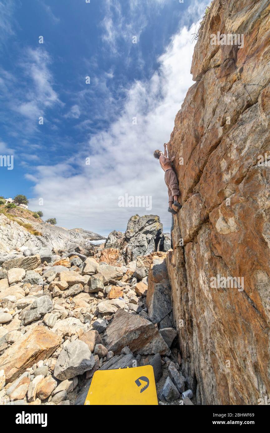 Grimpeur de roche mâle pratiquant le boulandrage sans corde sur un bloc devant la mer. Un bloc élevé pour les gens avec ténacité et confiance Banque D'Images