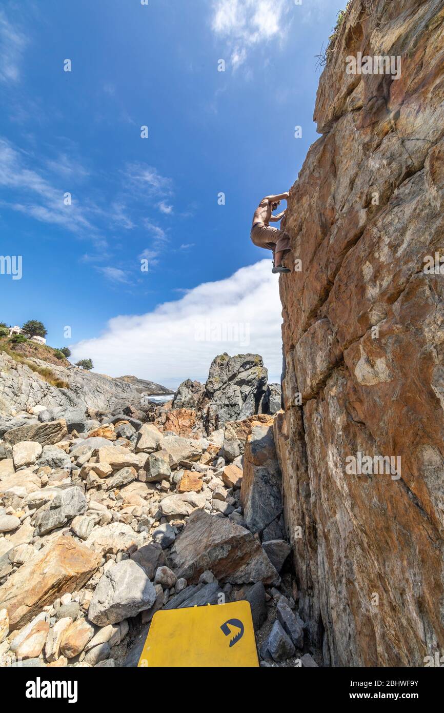 Grimpeur de roche mâle pratiquant le boulandrage sans corde sur un bloc devant la mer. Un bloc élevé pour les gens avec ténacité et confiance Banque D'Images