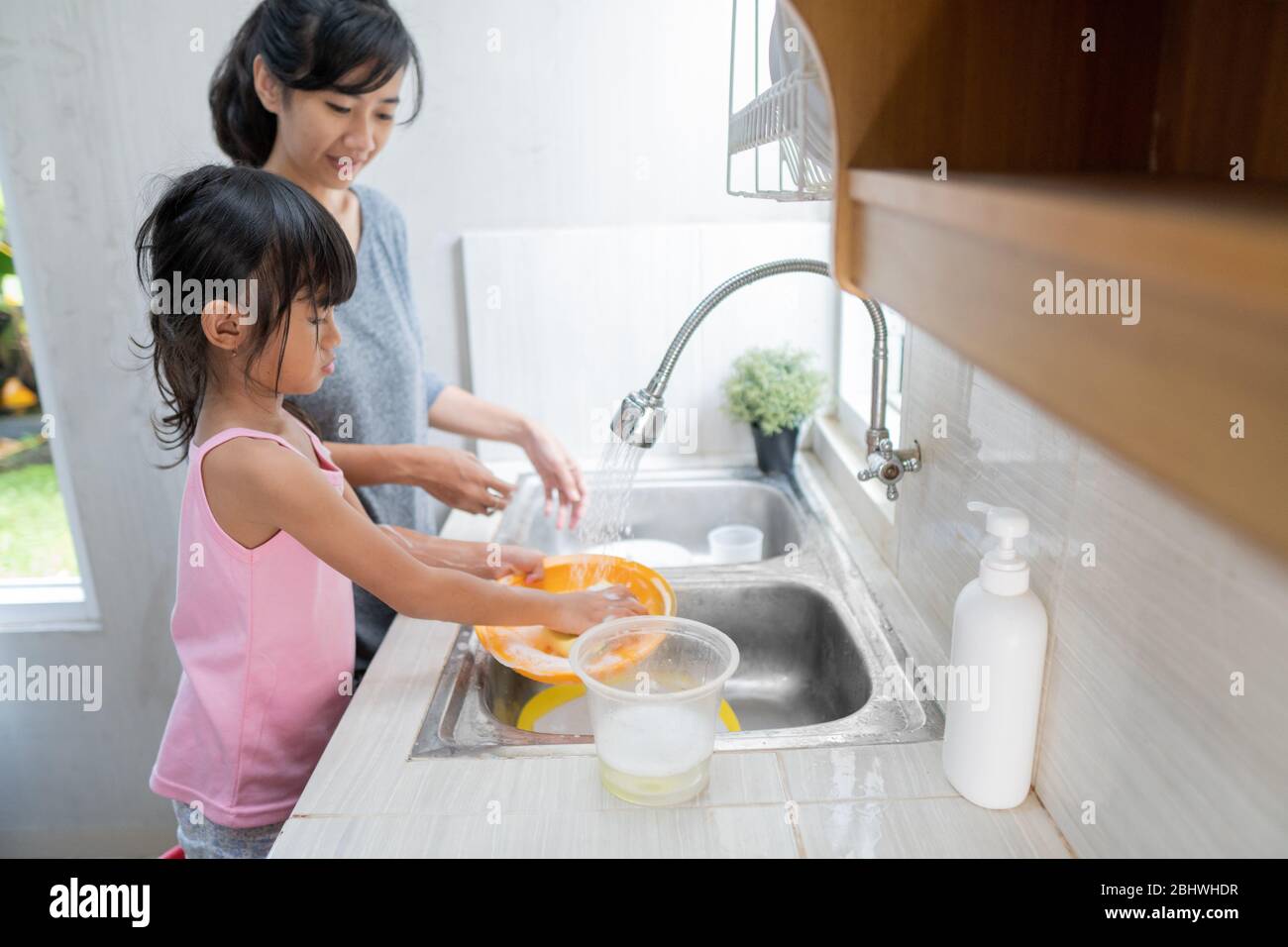 Fille asiatique aidant sa mère dans la cuisine laver les plats ensemble Banque D'Images