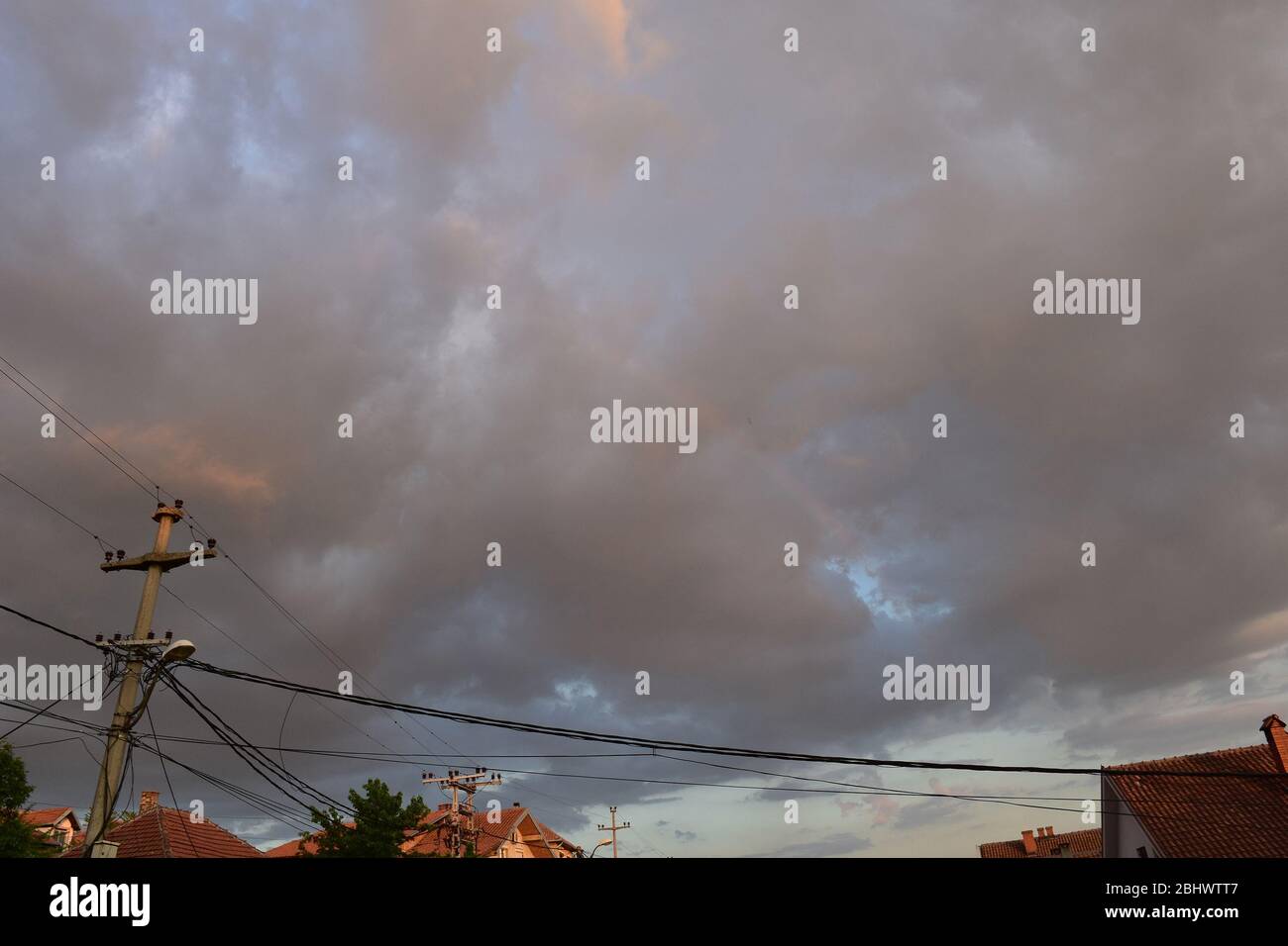 Au-dessus des toits éclairés sont des nuages gris avec un arc-en-ciel long et fin Banque D'Images