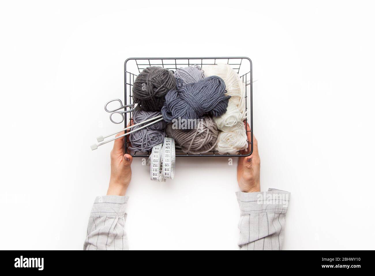 Les mains féminines tiennent un panier en métal noir avec du fil pour le tricot de gris et de blanc. Banque D'Images