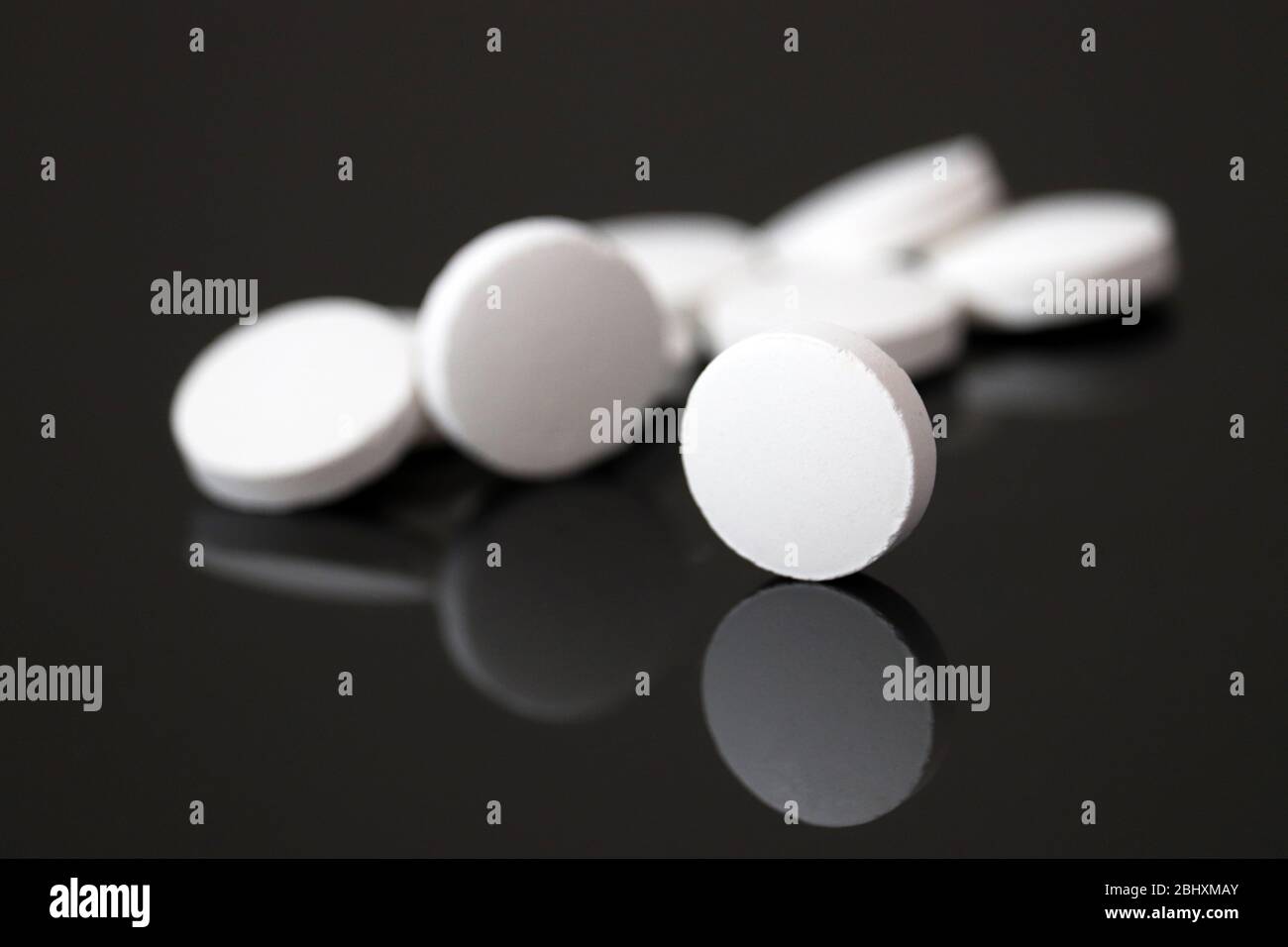 Les pilules blanches sont reflétées dans le verre foncé, les comprimés sur fond noir. Concept de pharmacie, de médicament ou de vitamines Banque D'Images
