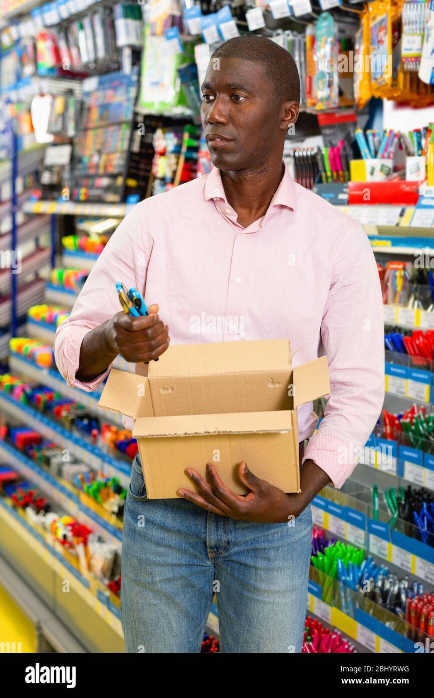 Joyeux homme afro-américain positif choisissant des fournitures de bureau à la papeterie département de supermarché Banque D'Images