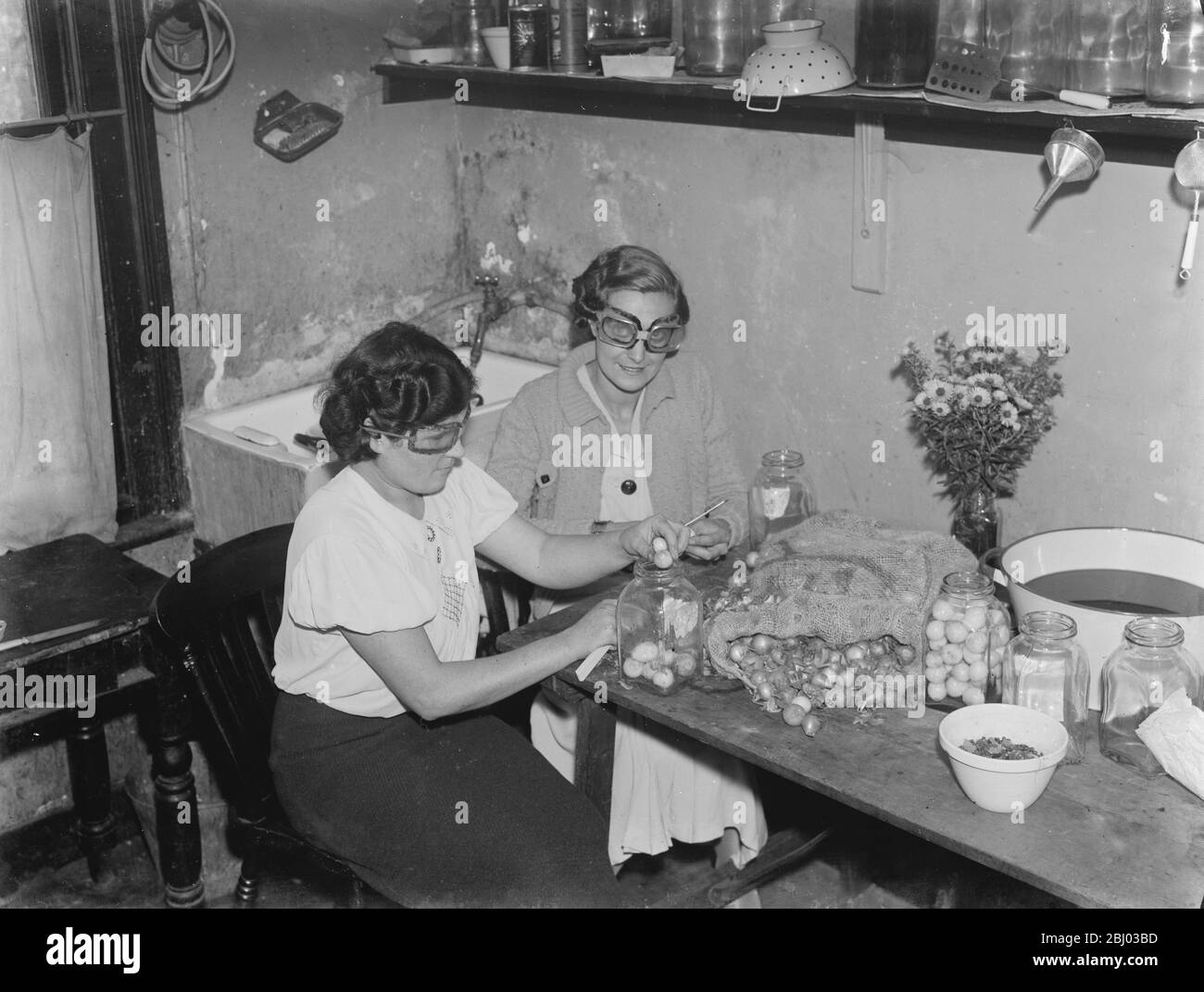 Miss Muriel Haten et Miss Irons pelant les oignons tout en portant des lunettes pour les arrêter de pleurer . - 1938 - Banque D'Images