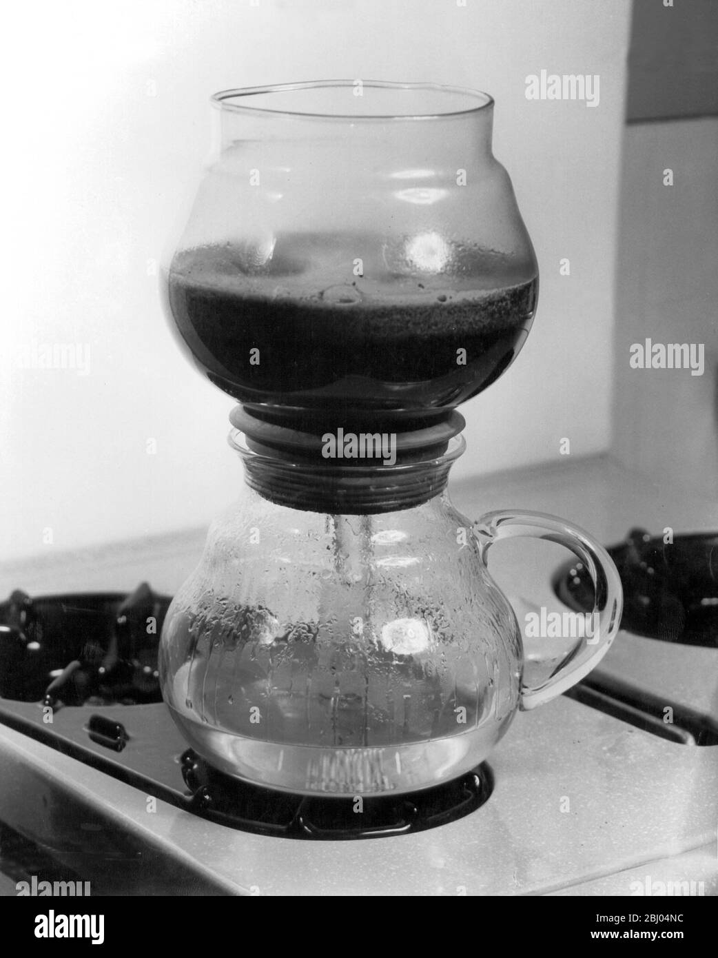 La cafetière des années 1950 - tandis que l'eau chauffe, elle force son chemin dans le bol supérieur. L'eau sous l'extrémité du verre reste dans la verseuse et empêche ainsi la verseuse d'ébullition et d'endommager le verre. Banque D'Images