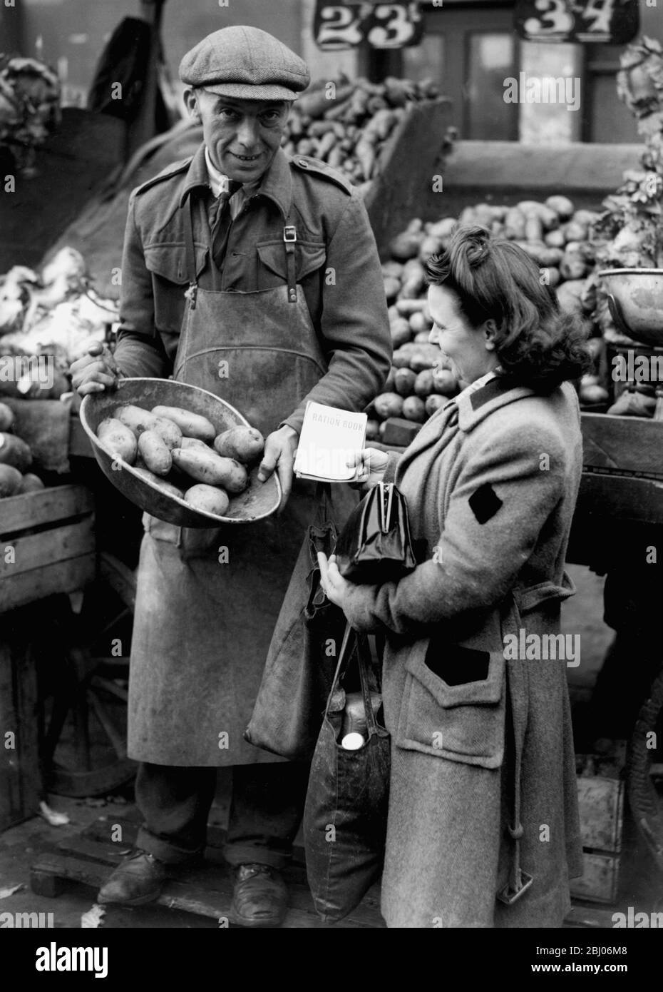 L'humble pomme de terre a rationné en Grande-Bretagne au taux de base de 3 lb par personne est entrée en vigueur en Grande-Bretagne hier. En raison de la sécheresse, des gelées printanières et des inondations, l'approvisionnement était un cinquième moins que 1946. Spectacles d'images: La scène dans un marché de Londres comme une femme de ménage achète deux semaines de ration, avec ses livres en main. - 10 novembre 1947. - Banque D'Images