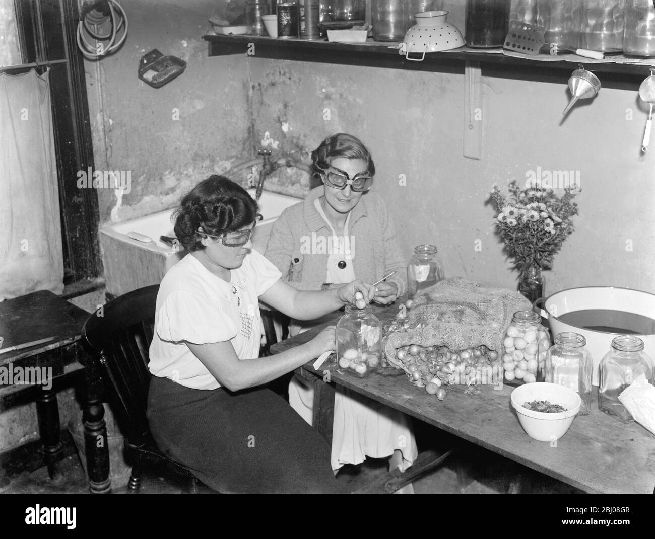 Miss Muriel Haten et Miss Irons pelant les oignons tout en portant des lunettes pour les arrêter de pleurer . - - 1938 - - Banque D'Images