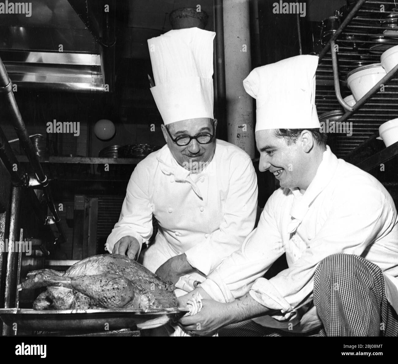 Auguste Laplanche, chef de l'hôtel Savoy, avec un chef junior tirant une dinde du four pour expliquer comment vous pouvez dire si c'est fait. - 26 novembre 1960 - Banque D'Images
