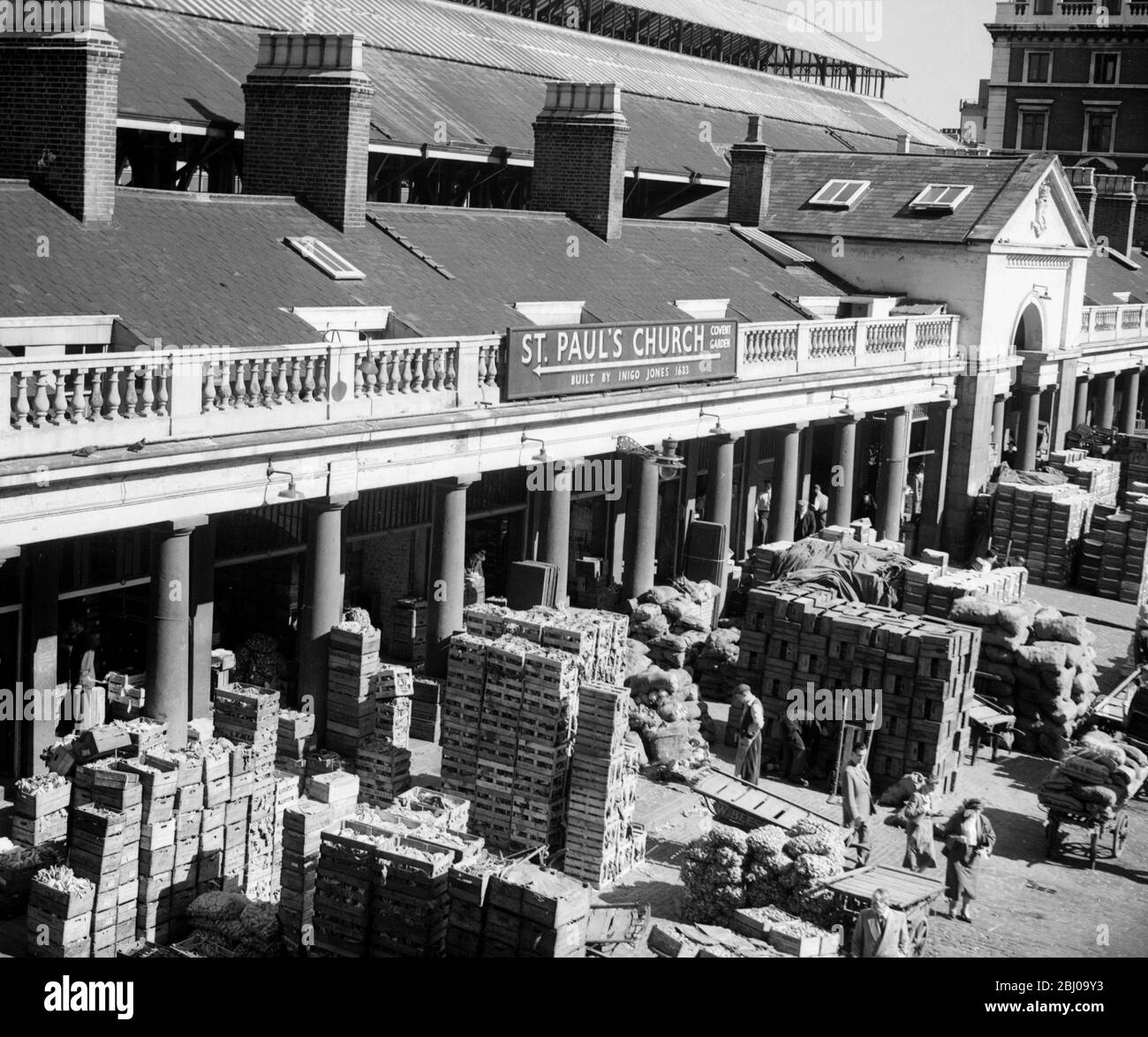 Chariots et boîtes remplis de fruits et légumes dans le marché des fleurs, des fruits et des légumes de Covent Garden . Un panneau donnant des indications vers l' église St Paul , Covent Garden , Londres , est vu sur le bâtiment . Fin des années 1940 , début des années 1950 Banque D'Images