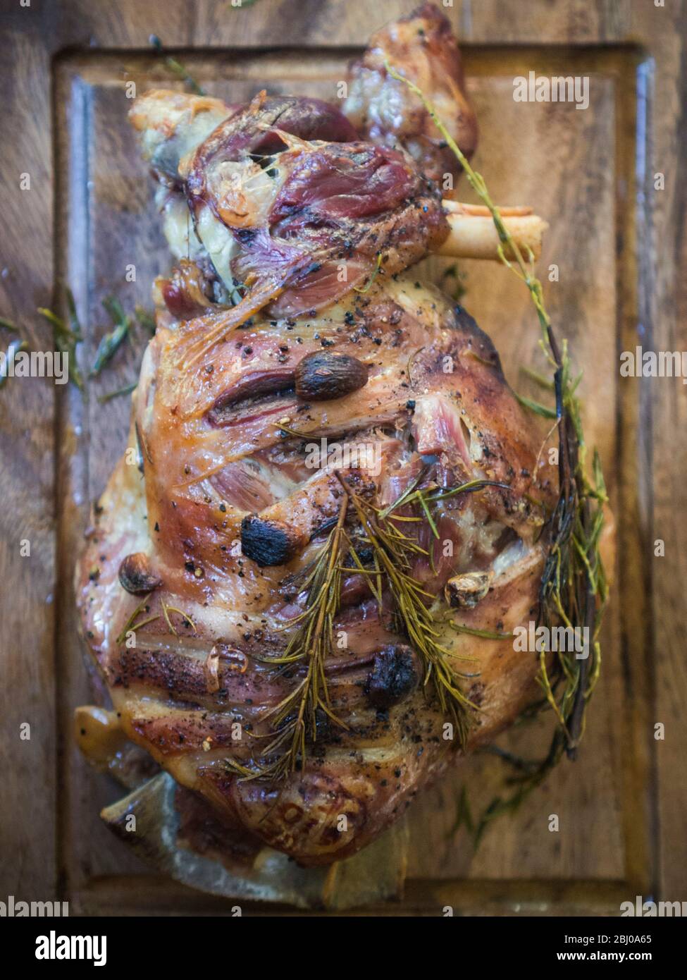 Épaule d'agneau rôtie lente avec ail et romarin, sur planche à découper en bois Banque D'Images