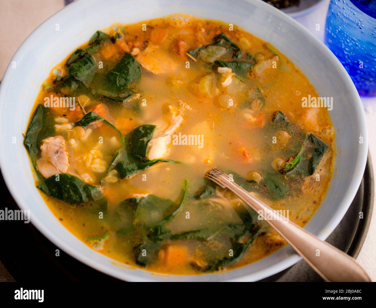 Repas complet Soupe de poulet, chorizo et légumes avec du riz brun, lentilles et épinards, servi dans un bol bleu pâle Banque D'Images