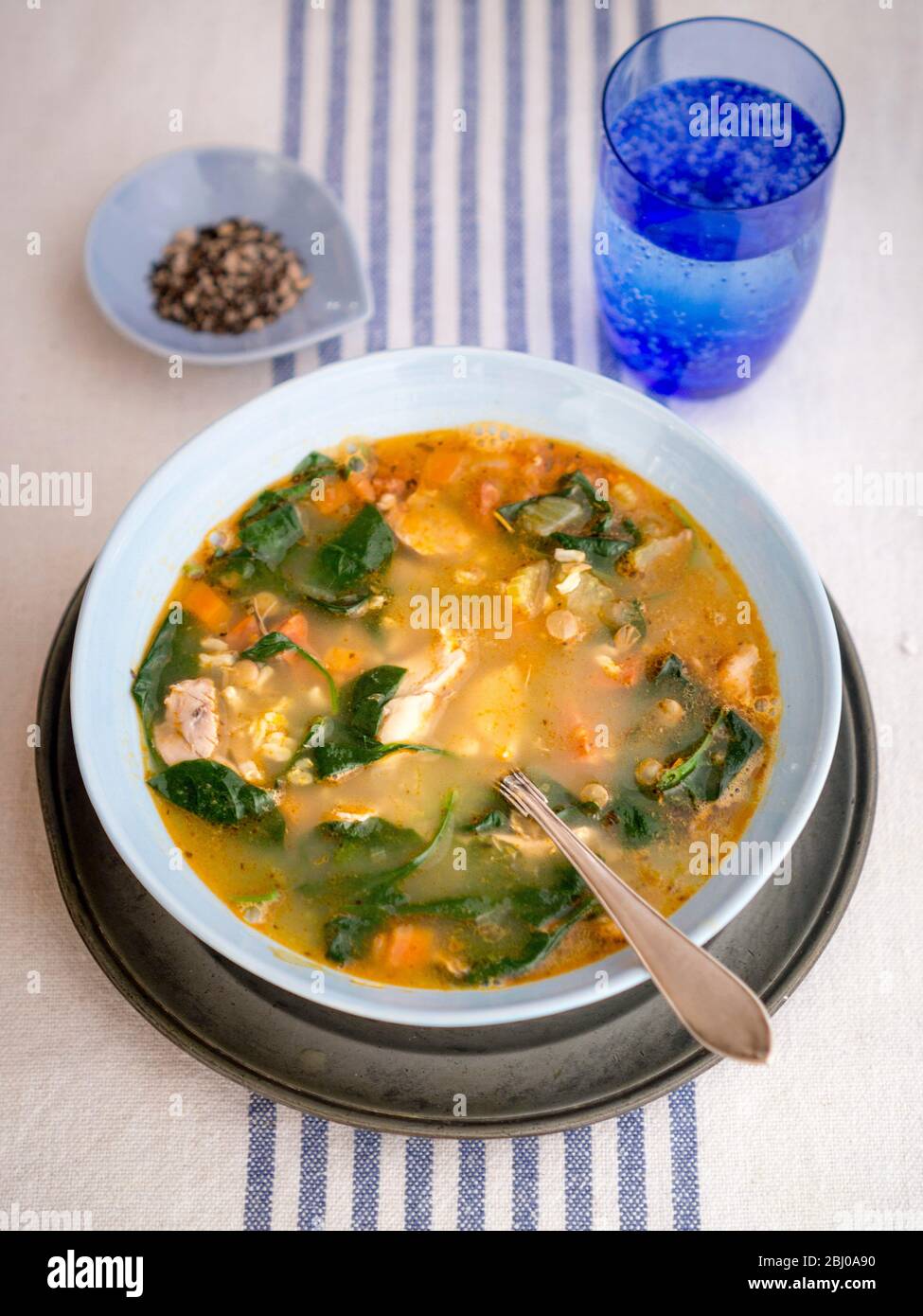 Repas complet Soupe de poulet, chorizo et légumes avec du riz brun, lentilles et épinards, servi dans un bol bleu pâle Banque D'Images