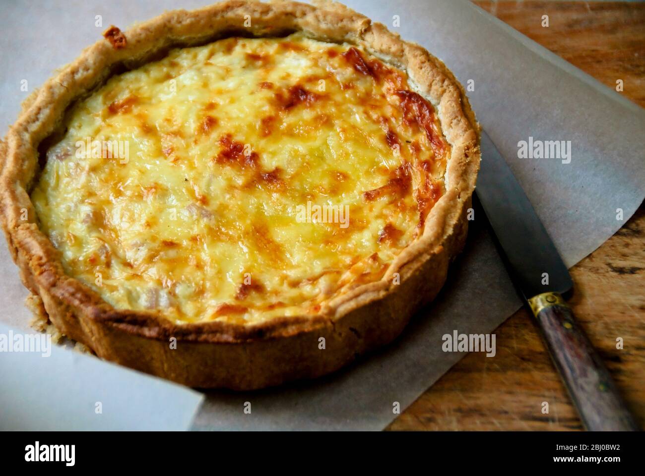 Petite quiche Lorraine sur papier sulfurisé avec couteau - Banque D'Images