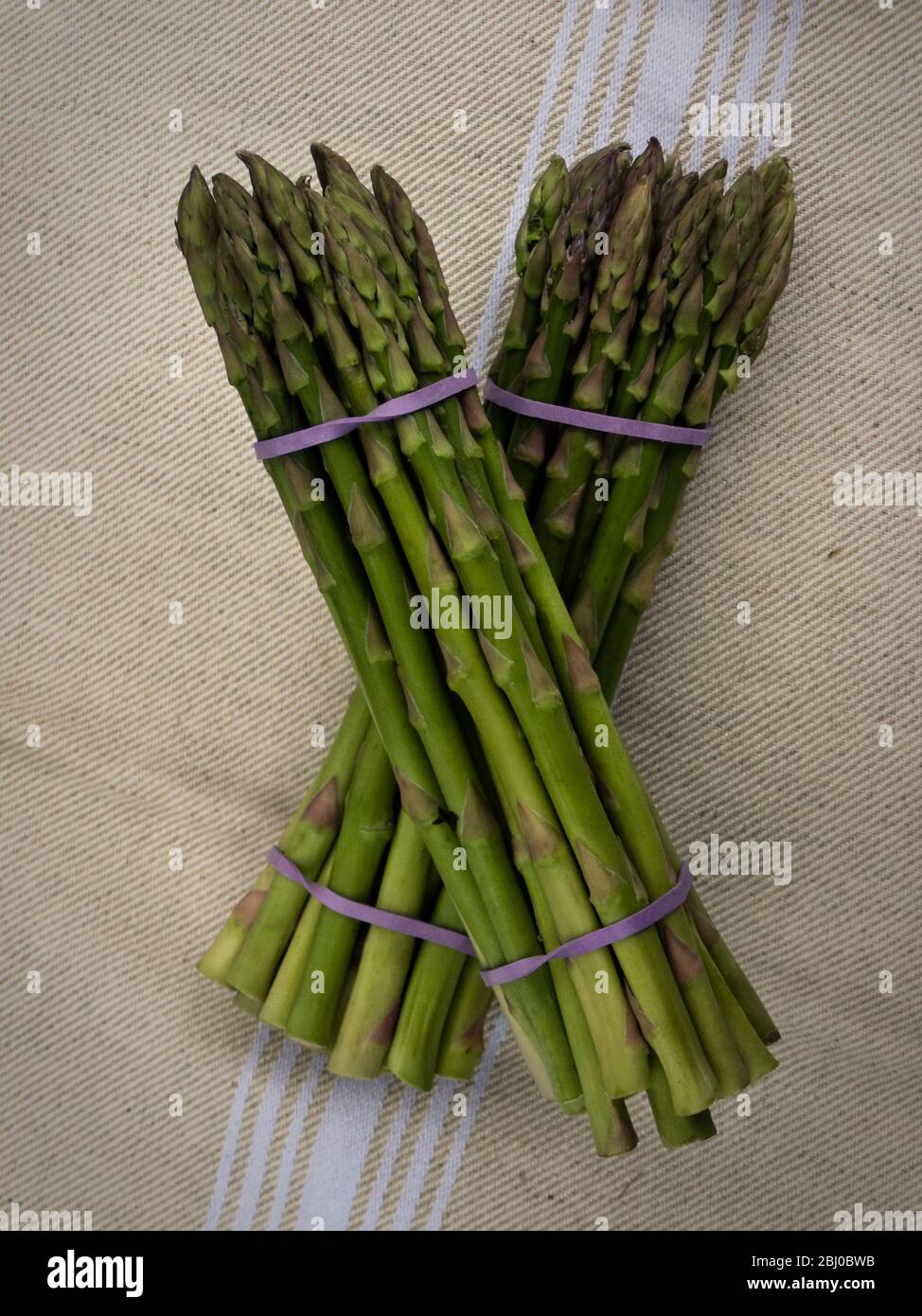 Deux paquets d'asperges anglaises fraîches sur plaque verte, prêtes à être cuites - Banque D'Images