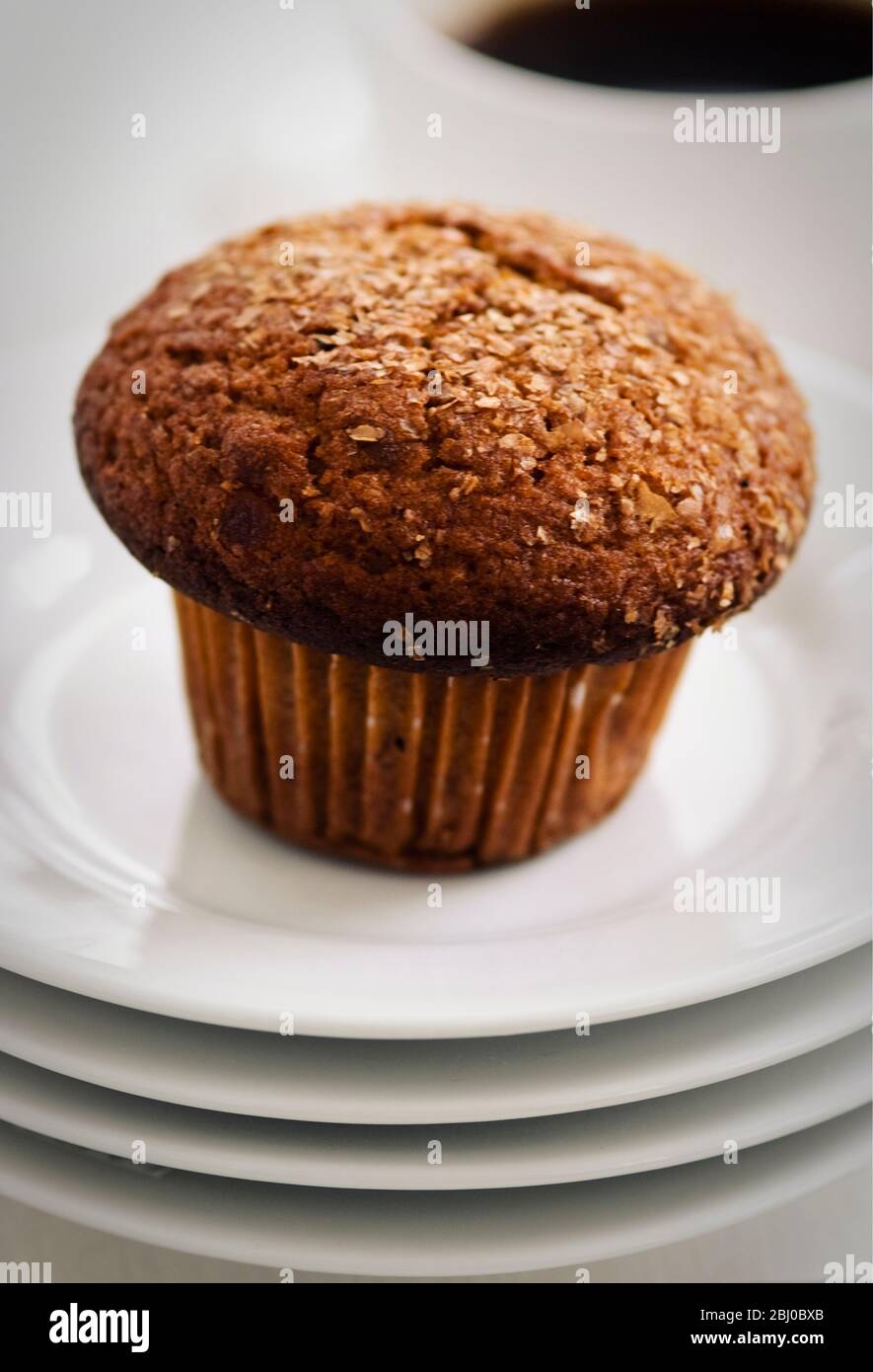 Muffin de son à la cannelle sur une pile de plaques blanches avec tasse de café noir - Banque D'Images