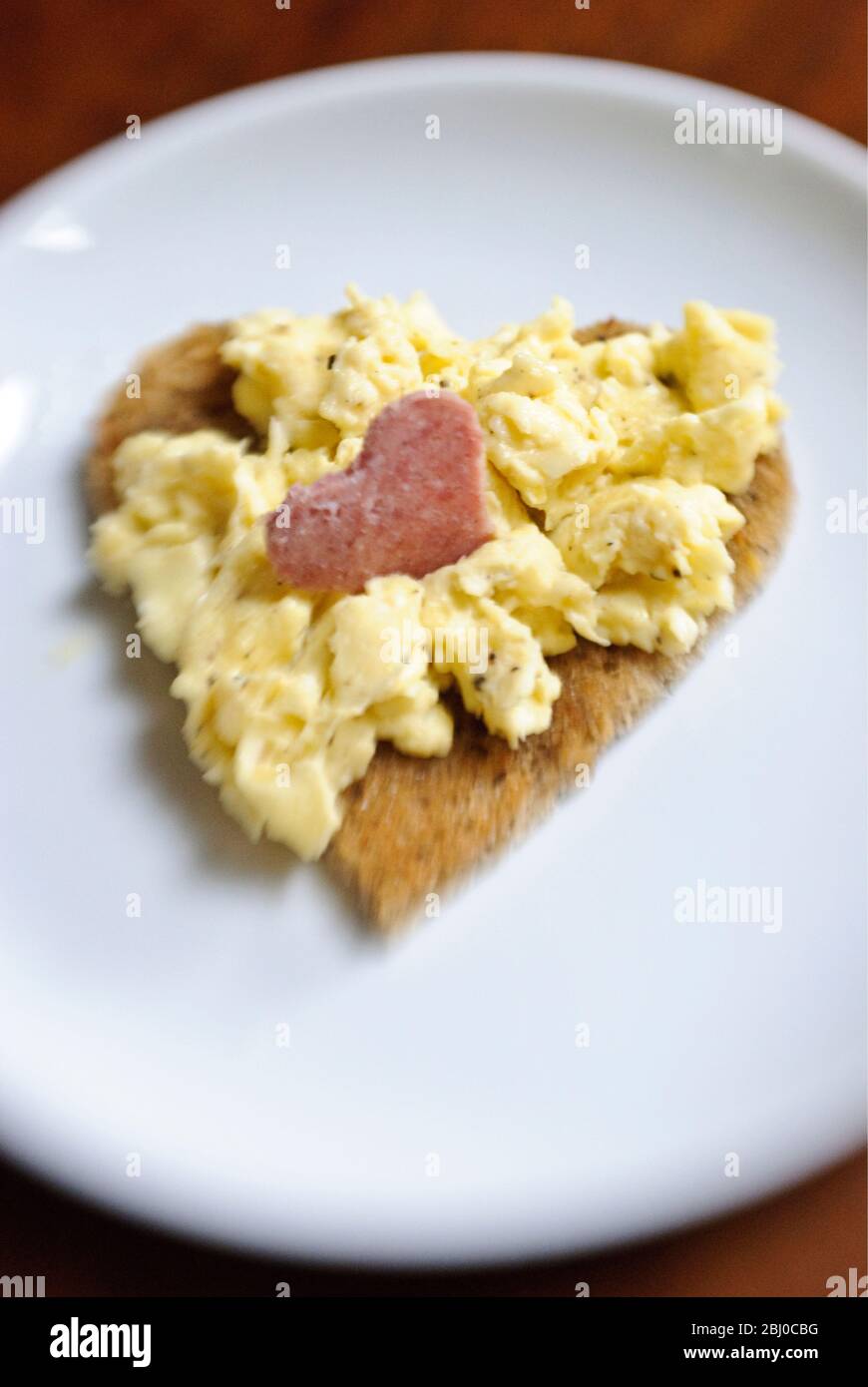 Saint-Valentin petit déjeuner d'œufs brouillés sur pain grillé en forme de coeur avec tranche de salami coupée en forme de coeur - Banque D'Images