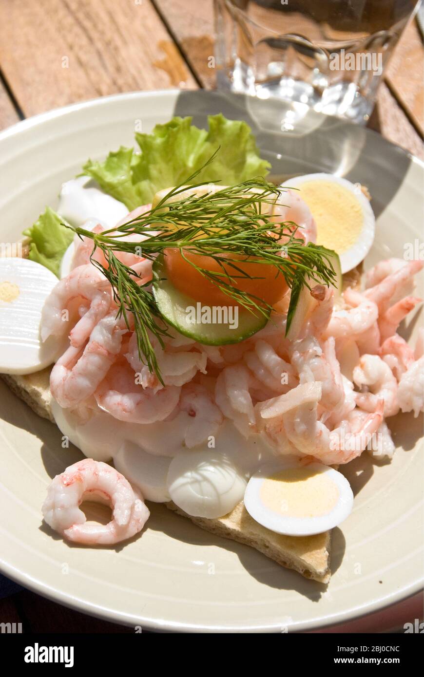Sandwich suédois ouvert aux crevettes fraîches, piquées sur du pain plat au foyer avec salade et mayonnaise, servi sur une table de café à l'extérieur - Banque D'Images
