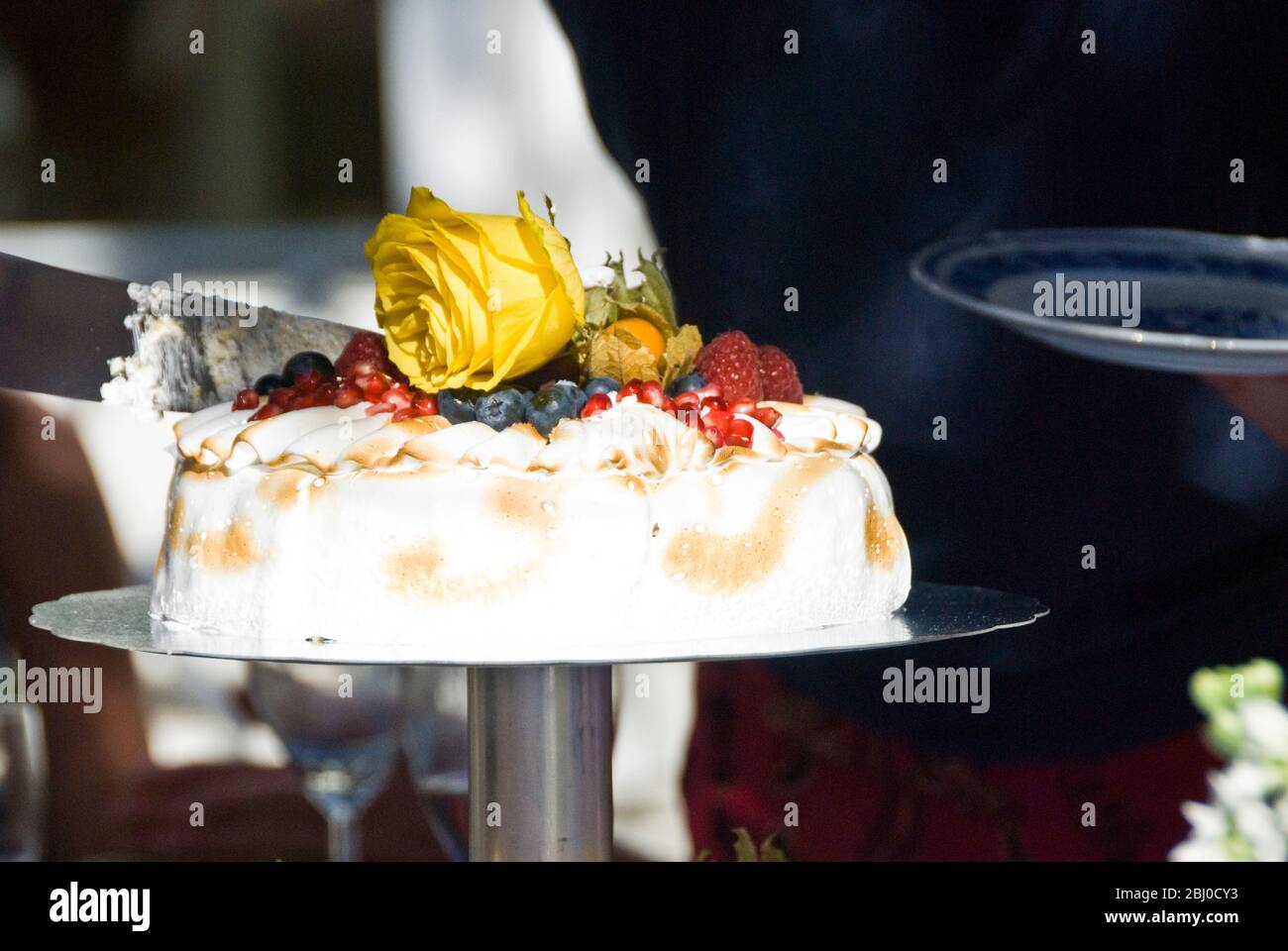 Gâteau de célébration de mousse de citron clair et de fruit de passion avec garniture de meringue douce, fruits exotiques frais et rose jaune coupé à l'extérieur en été Banque D'Images