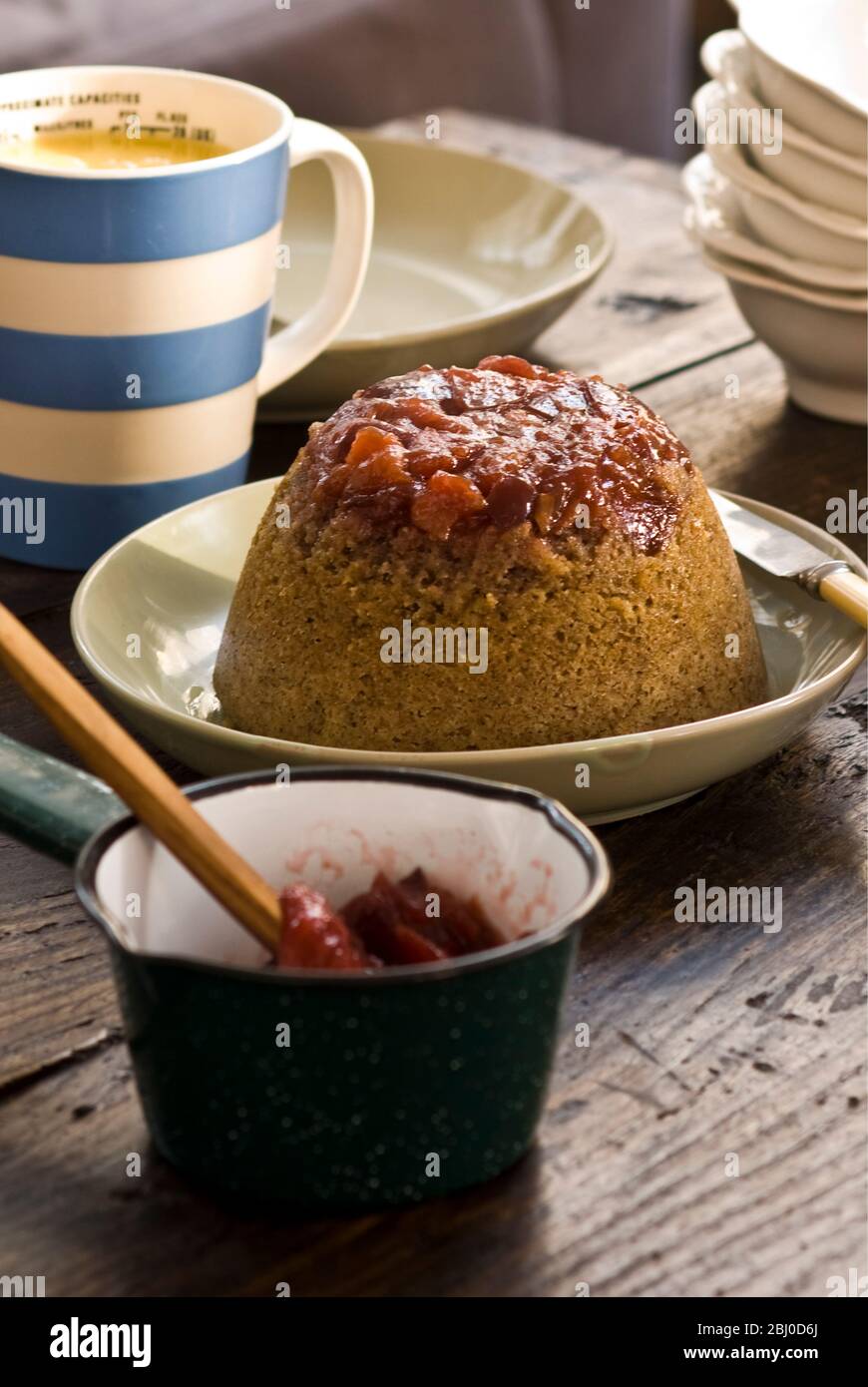 Pudding éponge traditionnelle à la vapeur avec des morses et compote de rhubarbe et crème anglaise, servi dans un cadre informel - Banque D'Images