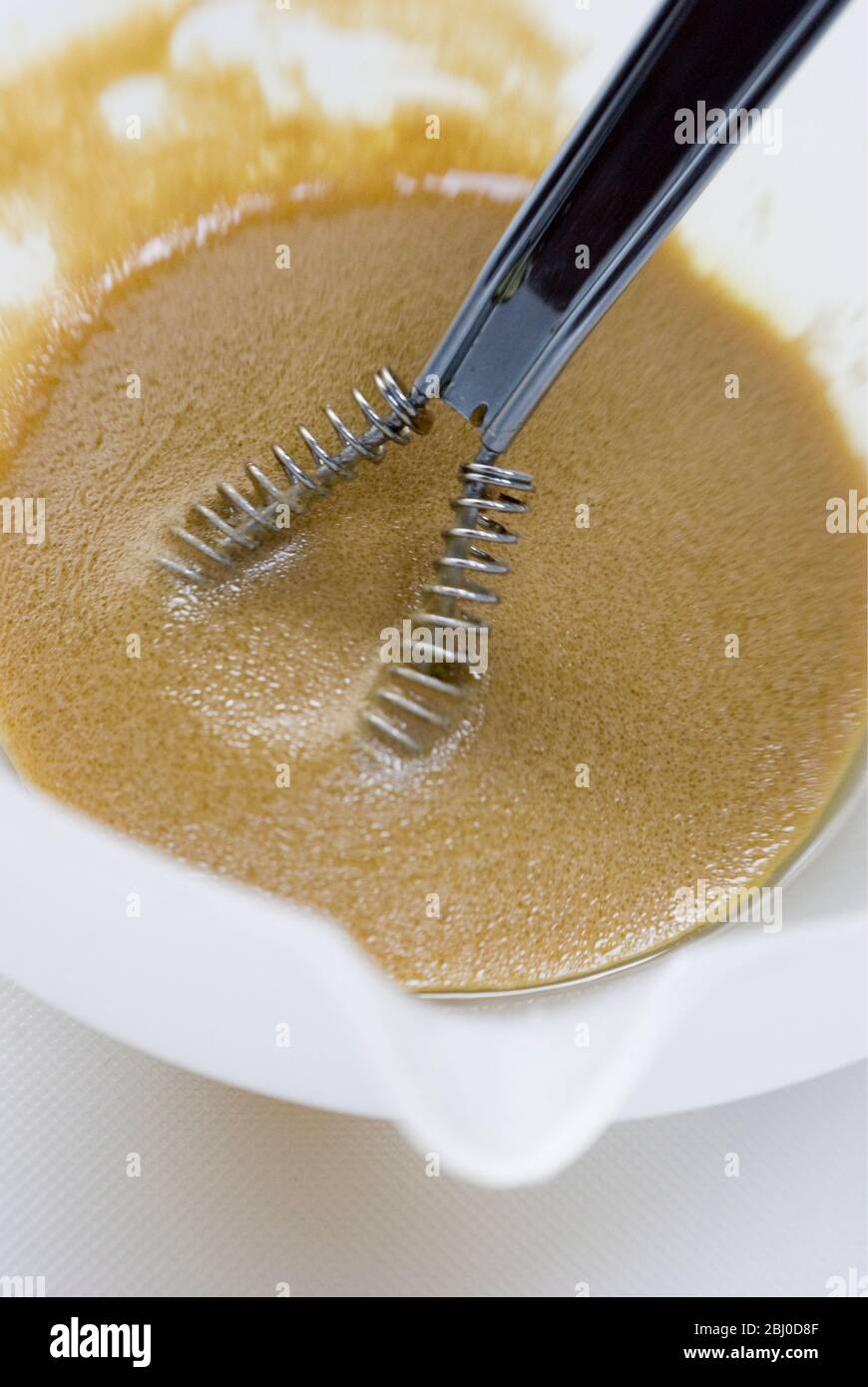 Fabrication d'une vinaigrette française classique avec de la moutarde, de l'huile d'olive et du vinaigre de vin rouge fouetté dans un bol blanc - Banque D'Images