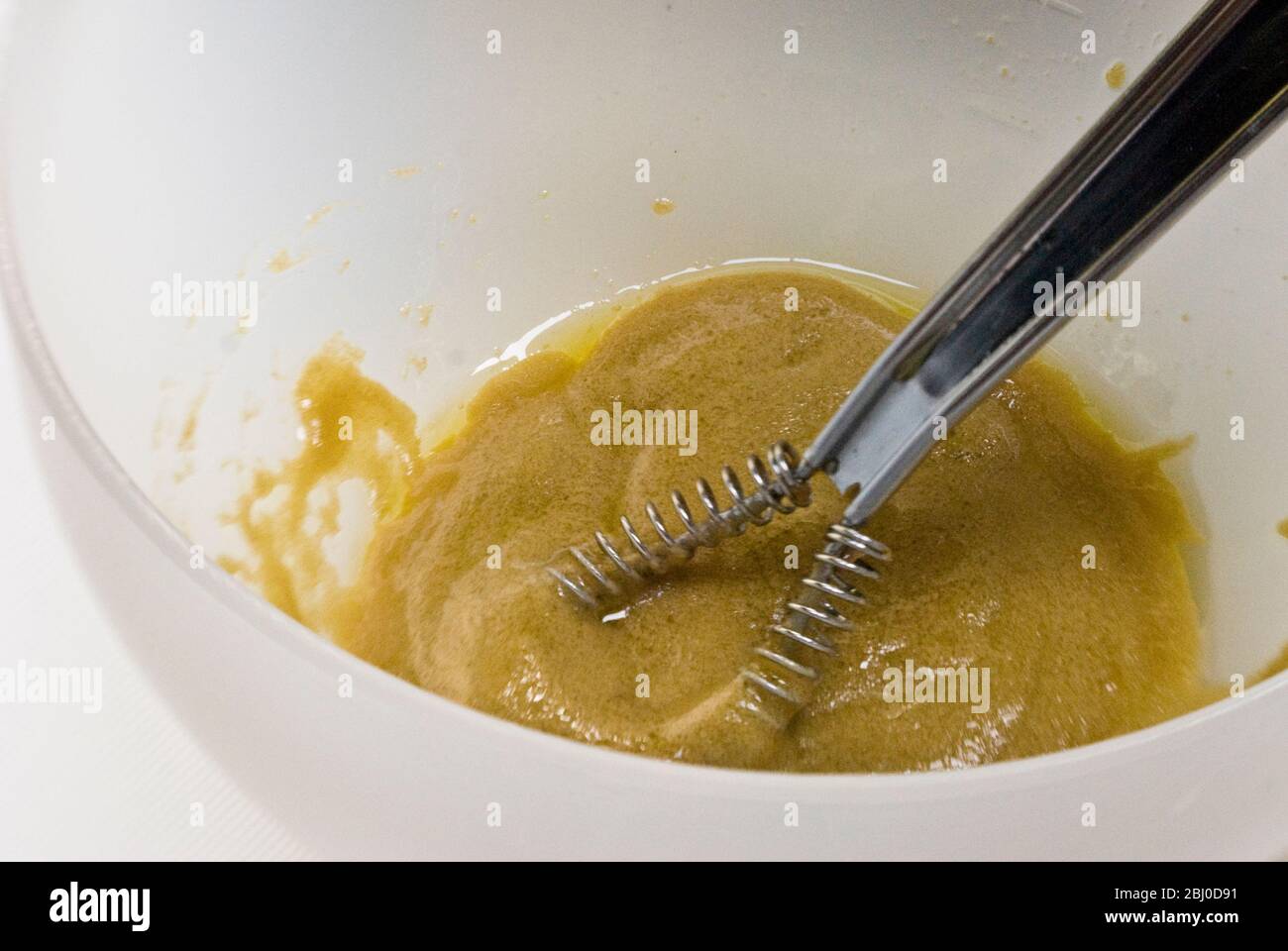 Fabrication d'une vinaigrette française classique avec de la moutarde, de l'huile d'olive et du vinaigre de vin rouge fouetté dans un bol blanc - Banque D'Images