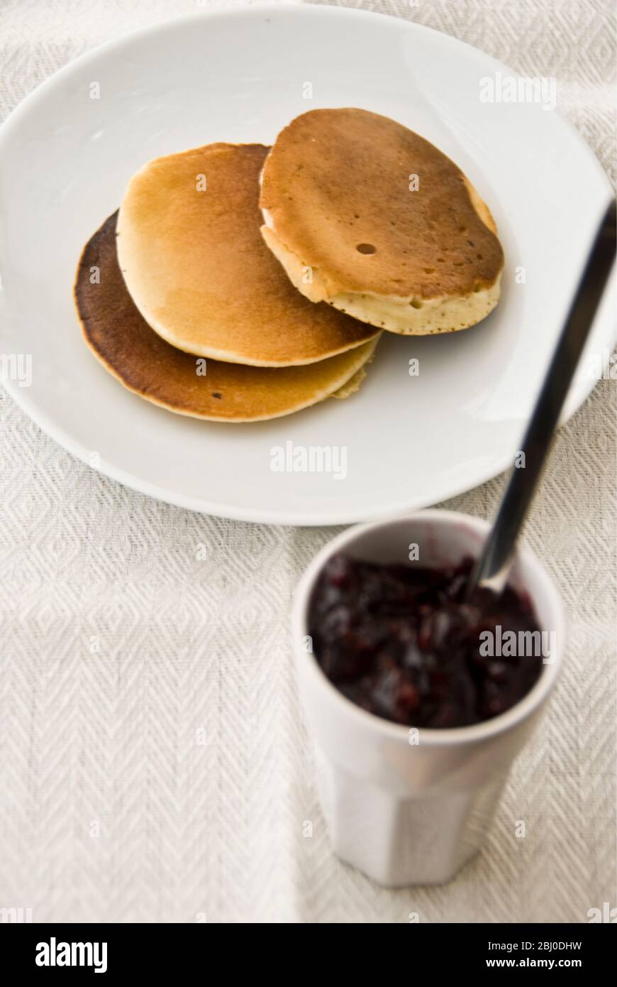 Trois crêpes Scotch sur une plaque blanche avec petit pot de confiture de framboises - Banque D'Images