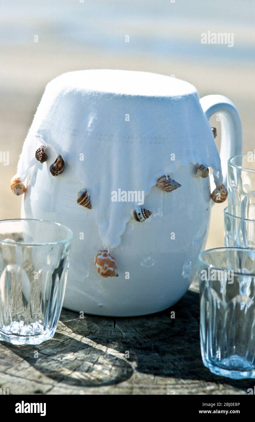 Pichet blanc avec couverture en tissu blanc pondérée avec coquilles de mer pour empêcher les insectes de s'en sortir. - Banque D'Images