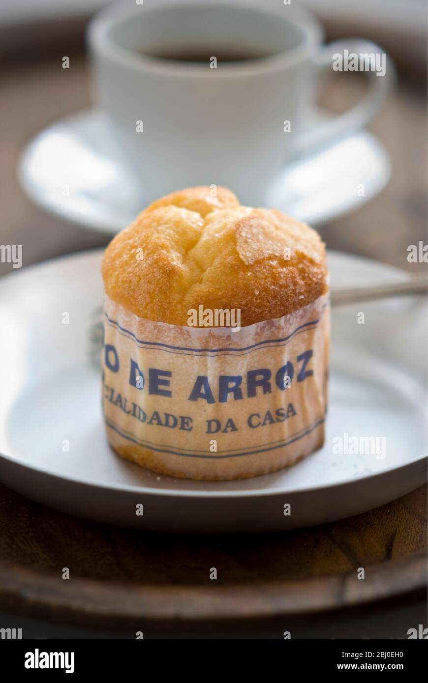 Gâteau de type muffin portugais classique fabriqué avec du riz dans un emballage en papier sur une plaque métallique, avec une tasse de café noir - Banque D'Images