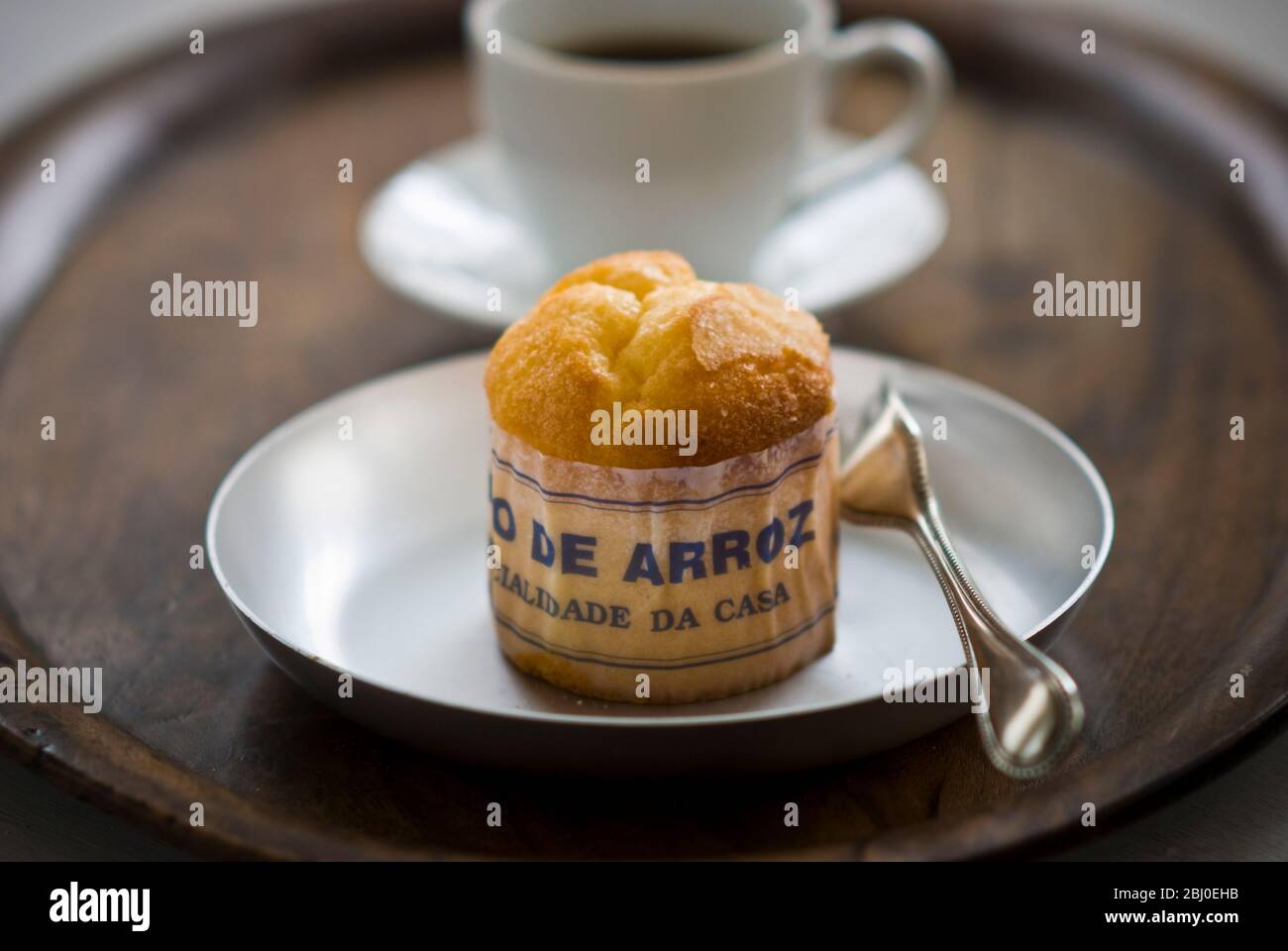 Gâteau de type muffin portugais classique fabriqué avec du riz dans un emballage en papier sur une plaque métallique, avec une tasse de café noir - Banque D'Images