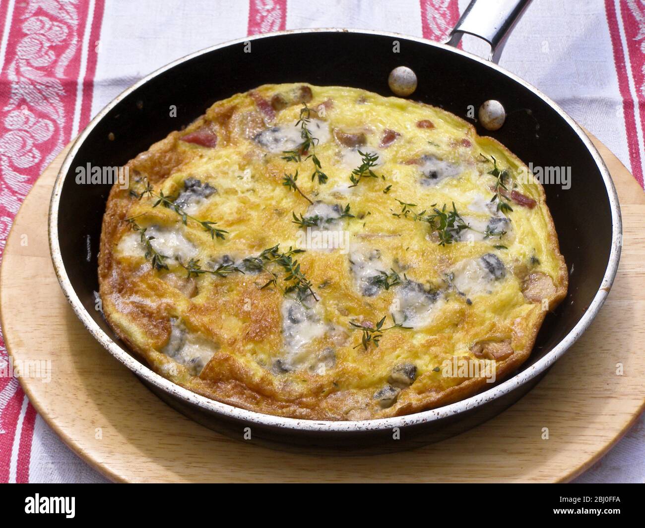 Frittata au fromage de chèvre, aux champignons et au thym, servis dans une poêle sur plaque en bois. - Banque D'Images