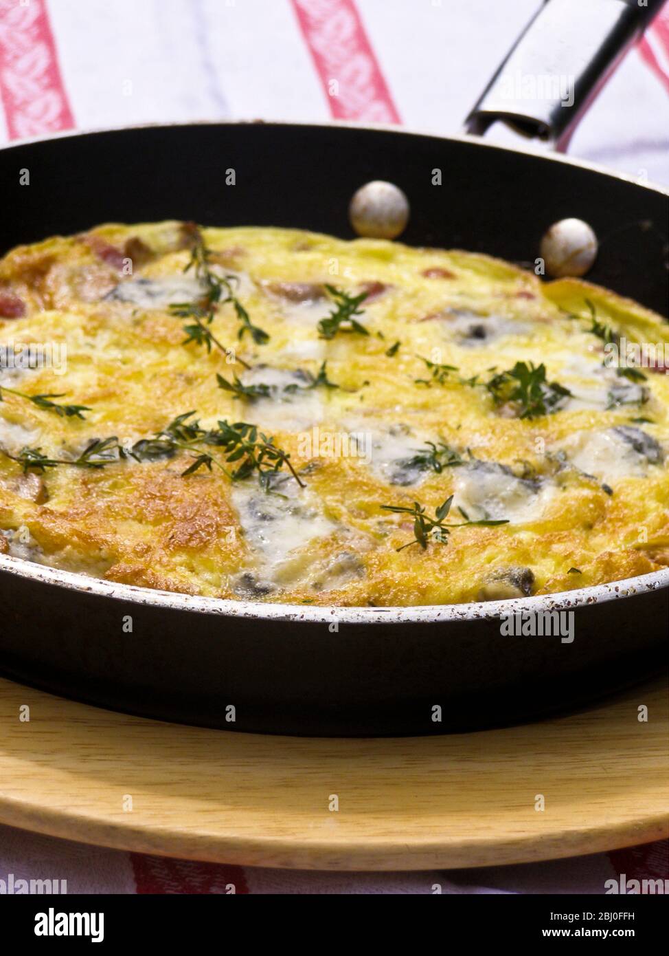 Frittata au fromage de chèvre, aux champignons et au thym, servis dans une poêle sur plaque en bois. - - Banque D'Images