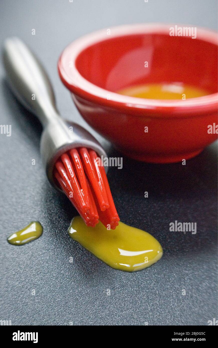 Jaune d'œuf dans un petit bol rouge et gouttes de silicone rouge 'pipis' de la brosse à pâtisserie moderne. - Banque D'Images