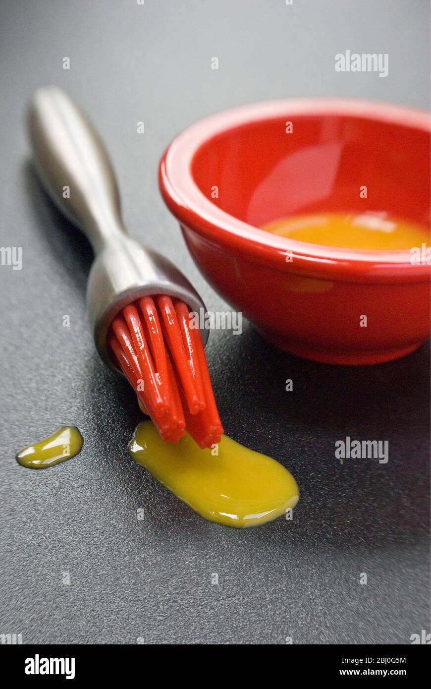 Jaune d'œuf dans un petit bol rouge et gouttes de silicone rouge 'pipis' de la brosse à pâtisserie moderne. - Banque D'Images