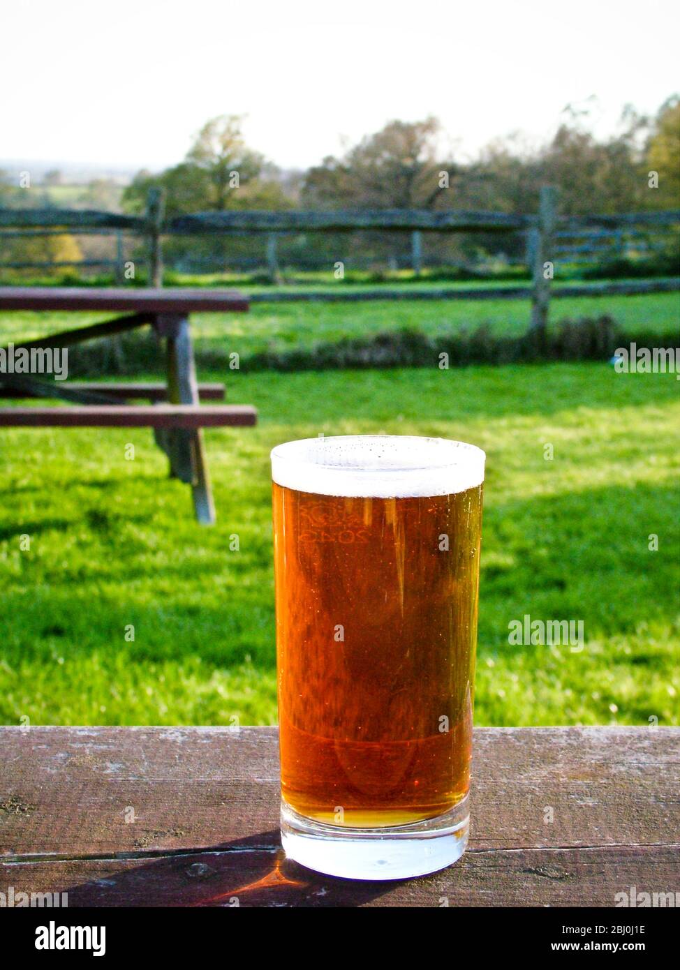 Verre de bière droit sur la table de jardin de pub le soir du printemps - Banque D'Images