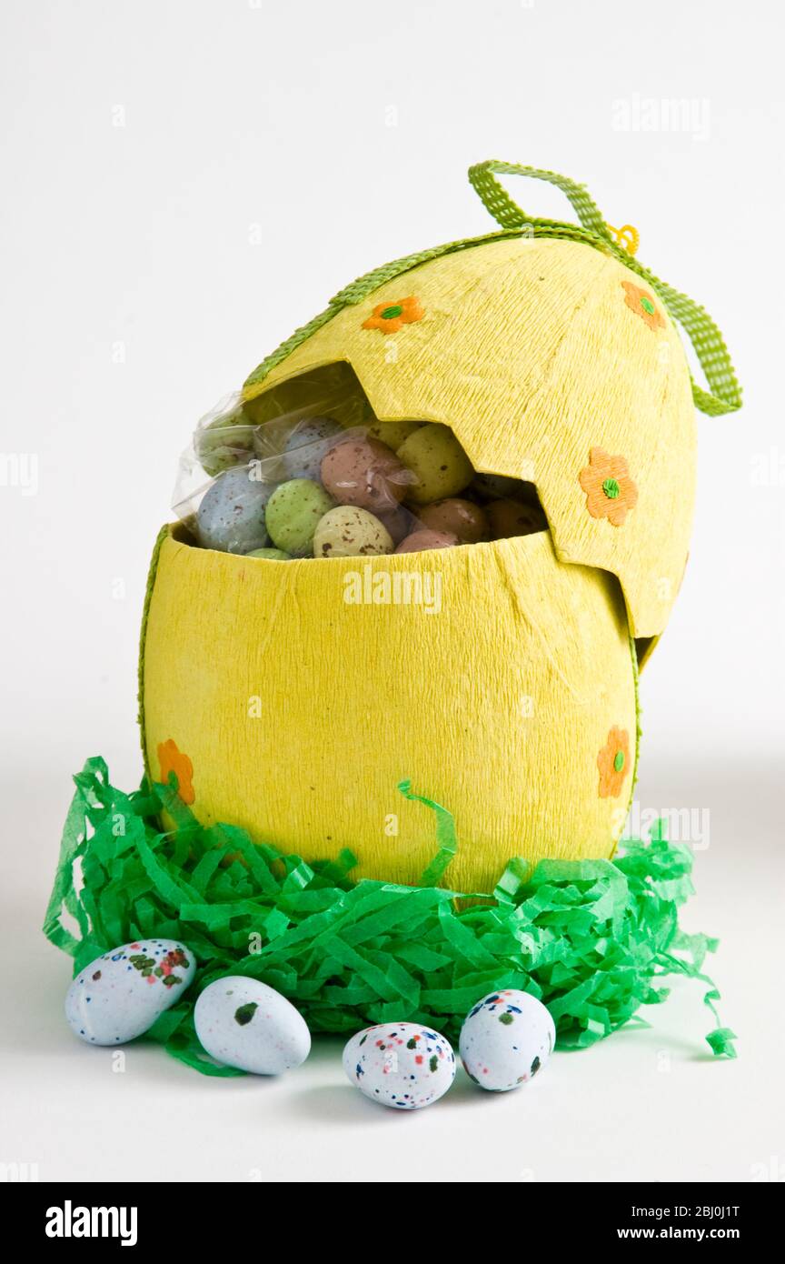 Boîte en papier décorée en forme d'oeuf avec œufs au chocolat enrobés de sucre Banque D'Images