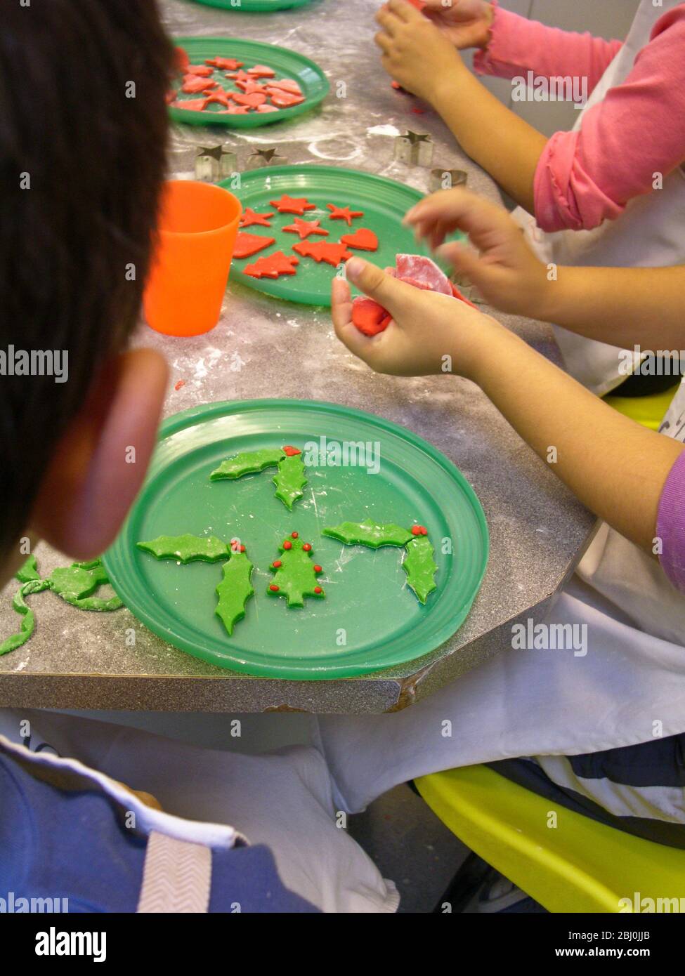 Enfants découpant des formes de Noël décoratives à partir de glaçage de couleur fondant pour décorer des gâteaux - Banque D'Images