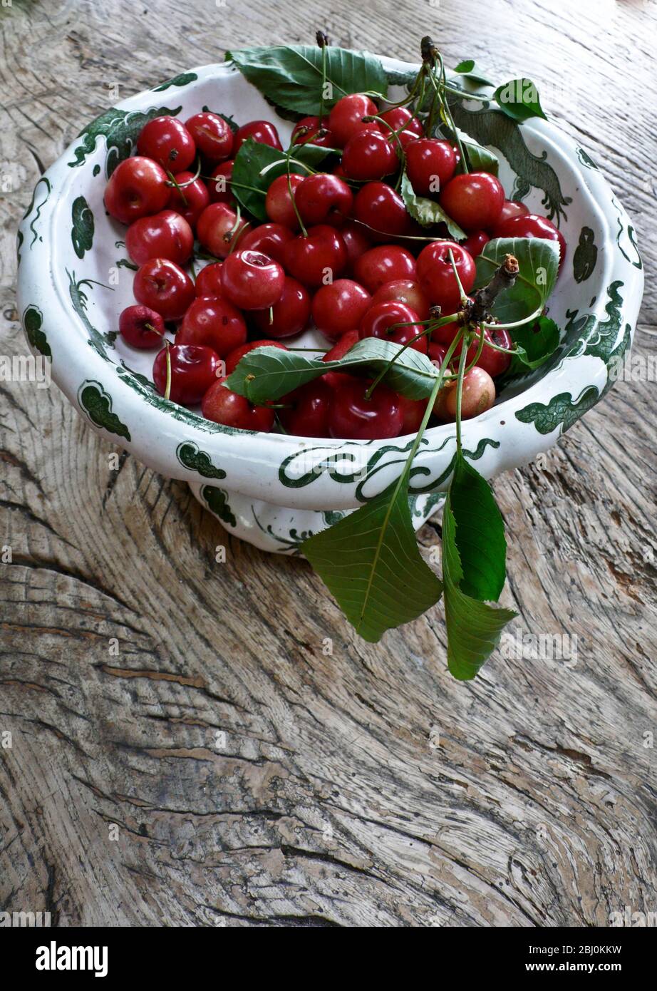 Cerises fraîchement cueillies dans un jardin Kentish dans un bol décoratif sur table en bois rustique - Banque D'Images