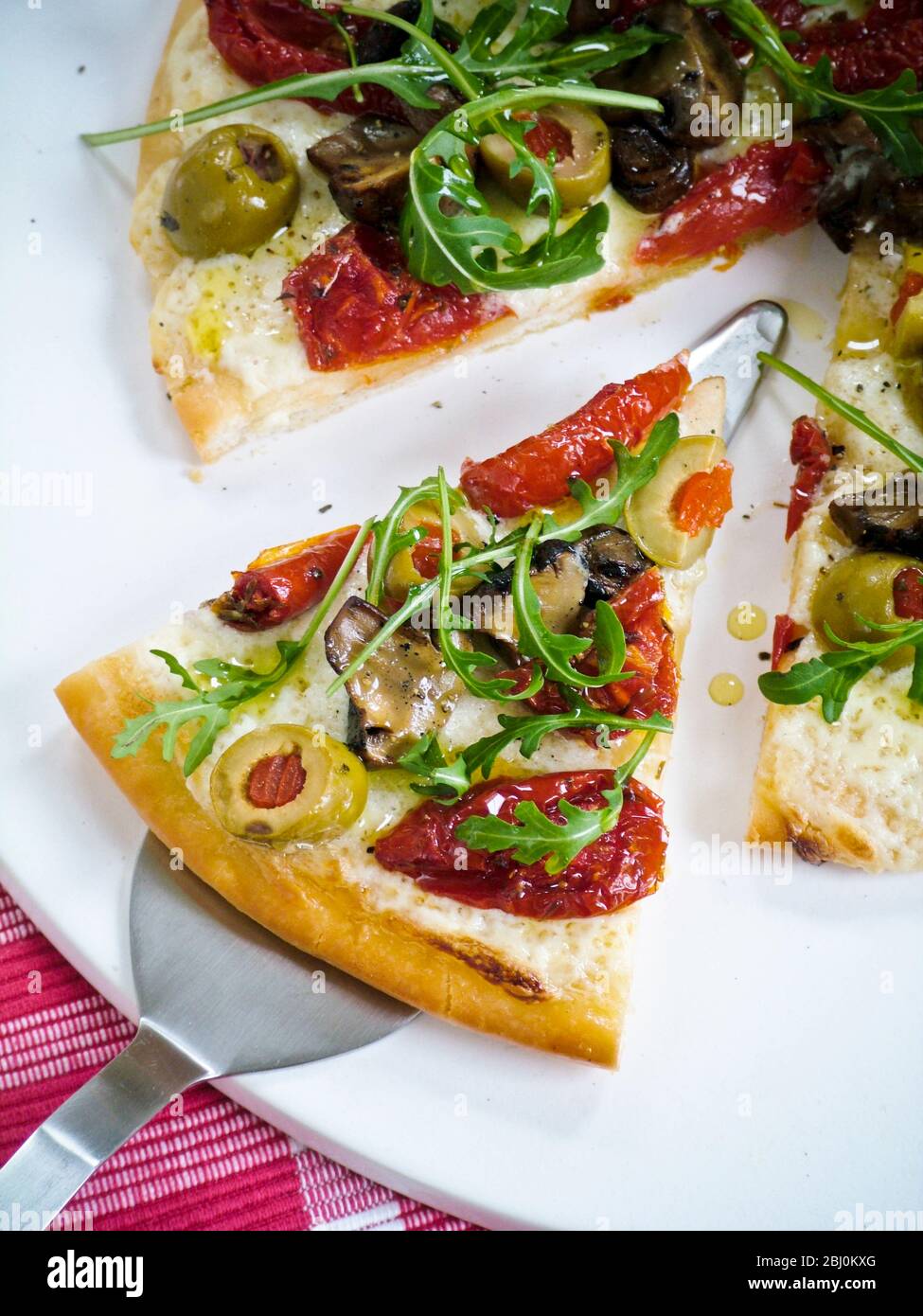 Pizza avec tomates séchées, aubergine, olives, mozzarella et roquette - Banque D'Images