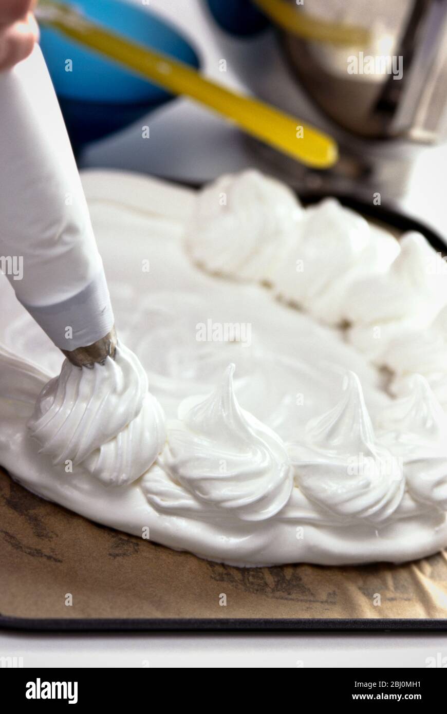 Piping meringue tourbillons autour du bord d'une base meringue pour faire un Pavlova classique - Banque D'Images