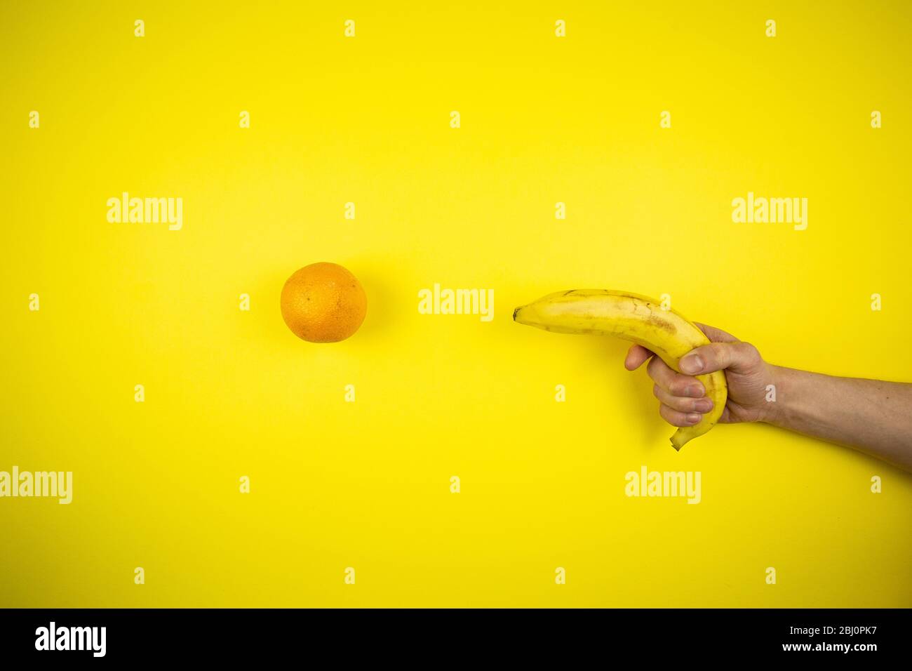 La banane prend une orange sur un fond jaune Banque D'Images