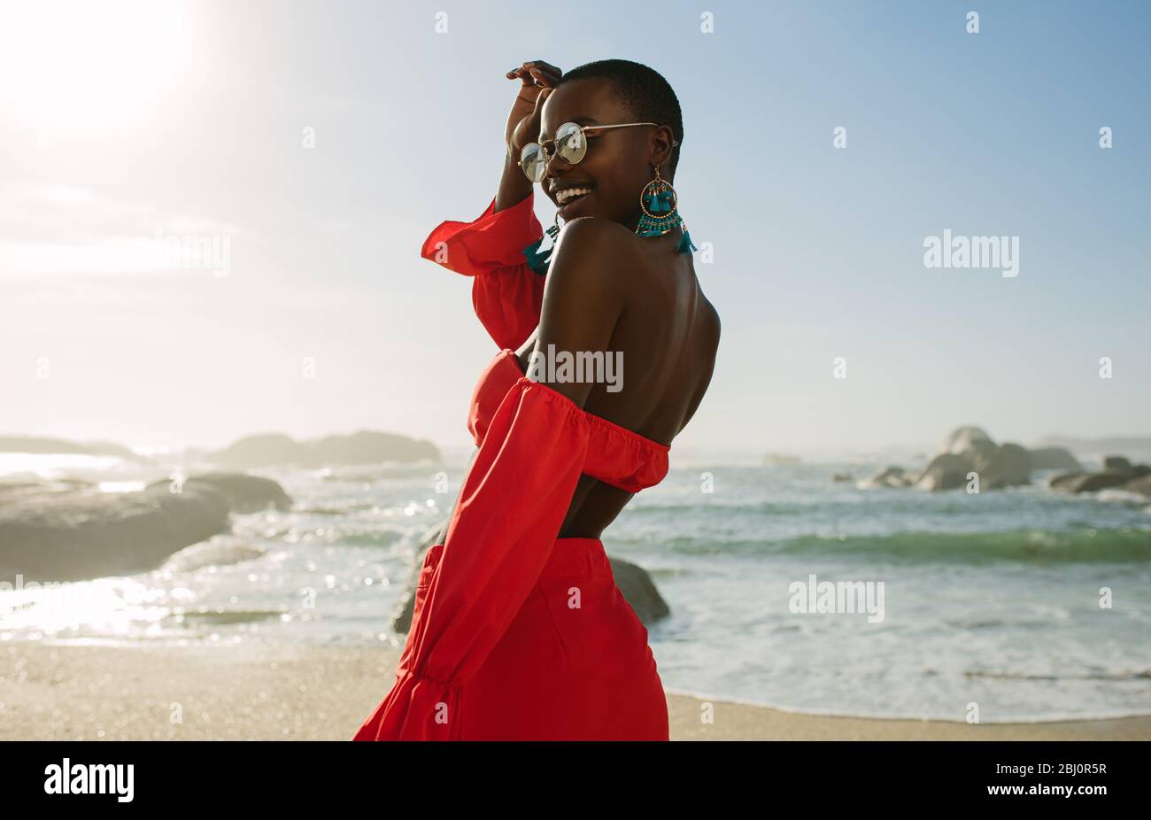 Belle femme africaine en robe rouge profitant sur la plage. Femme souriante dans une belle robe marchant le long de la rive. Banque D'Images
