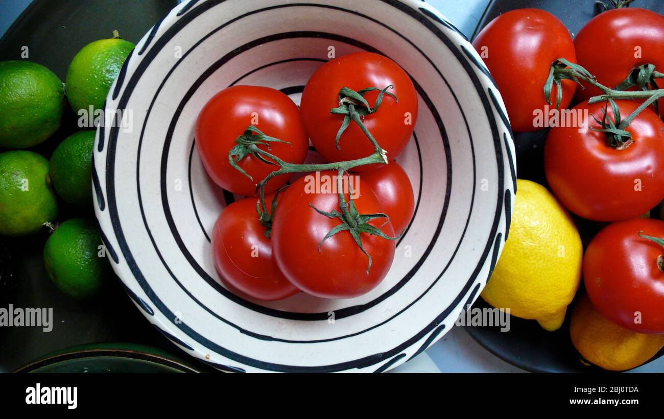 Tomates fraîches dans un bol en céramique moderne, plus un citron et des limes - Banque D'Images