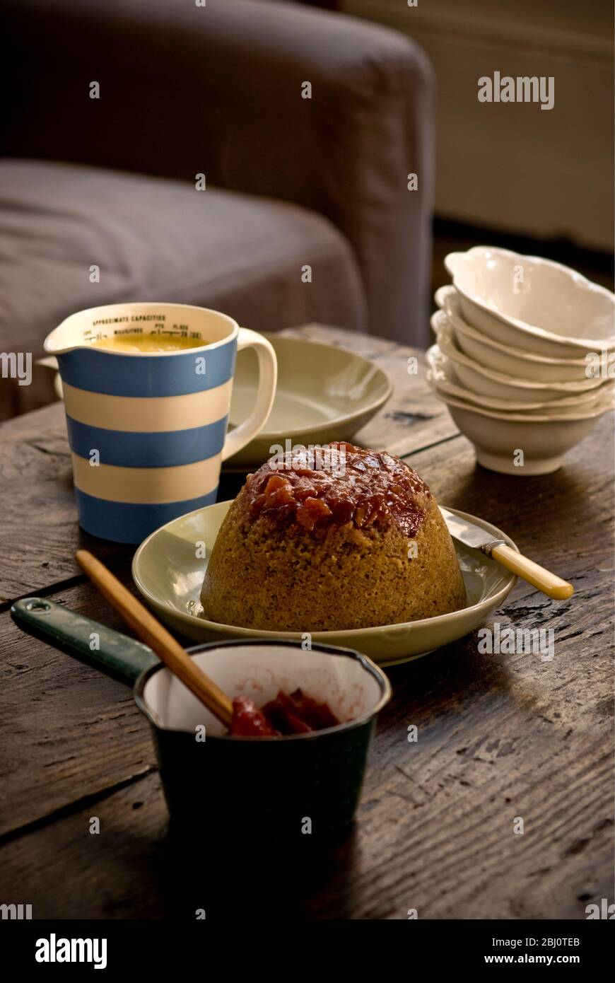 Pudding éponge traditionnelle à la vapeur avec des morses et compote de rhubarbe et crème anglaise, servi dans un cadre informel - Banque D'Images